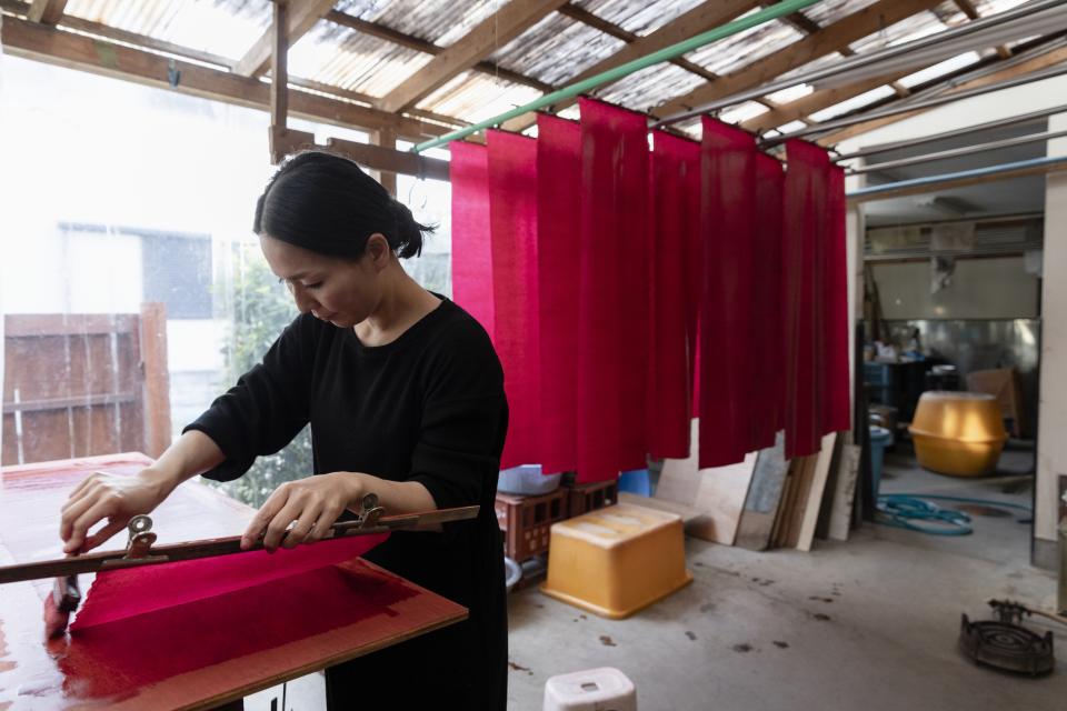 Artisan applying natural dye to fabric in a workshop, surrounded by vibrant red textiles hanging to dry.