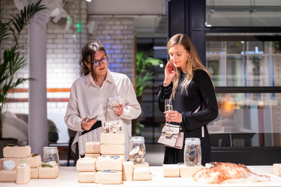 Two women engage with art pieces at the From The Ground Up exhibition, celebrating material innovation and creativity.