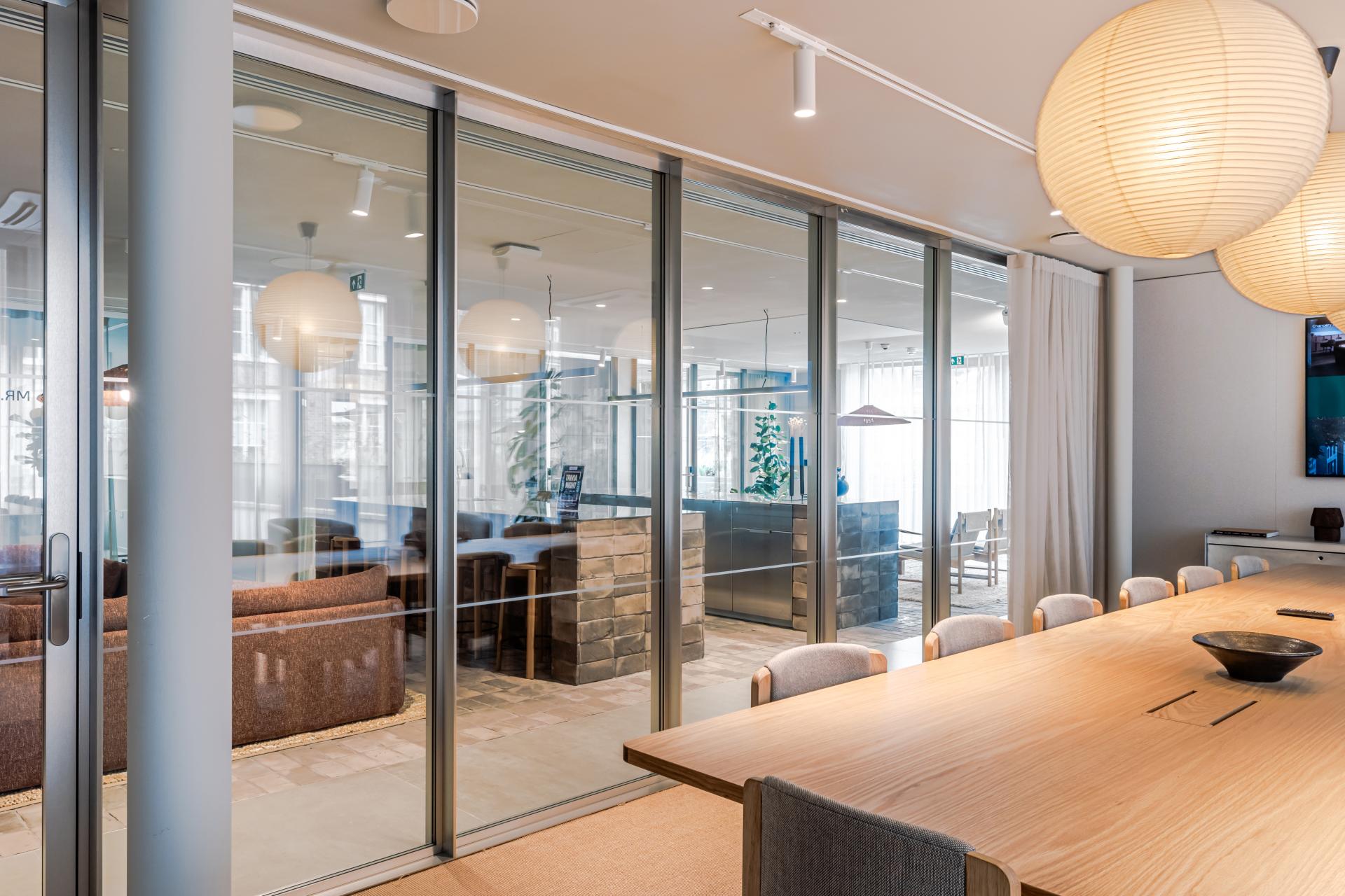 Contemporary workspace featuring glass partitions, wooden furniture, and comfortable seating areas, promoting flexibility and wellbeing.