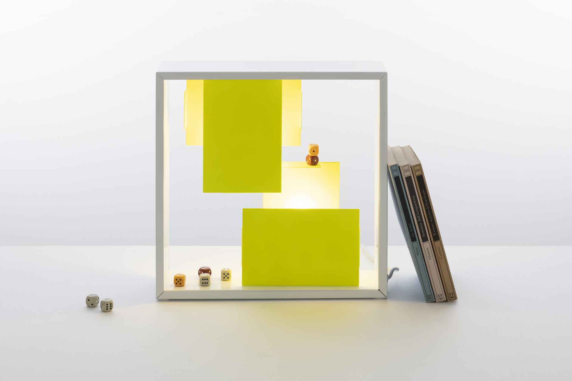 Bright, modern Tolomeo Micro lamp in yellow and white displayed with books and playful dice.