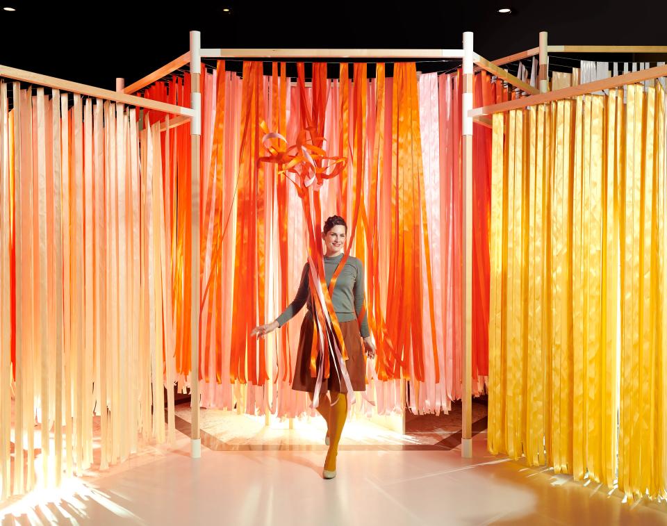 A woman walks through a vibrant installation of flowing ribbons in shades of orange and yellow, showcasing food and design collaboration.