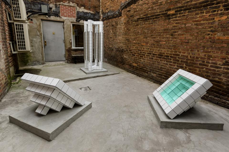 Sculptures by artist Zac Hacmon made of subway tiles displayed in an urban courtyard setting.