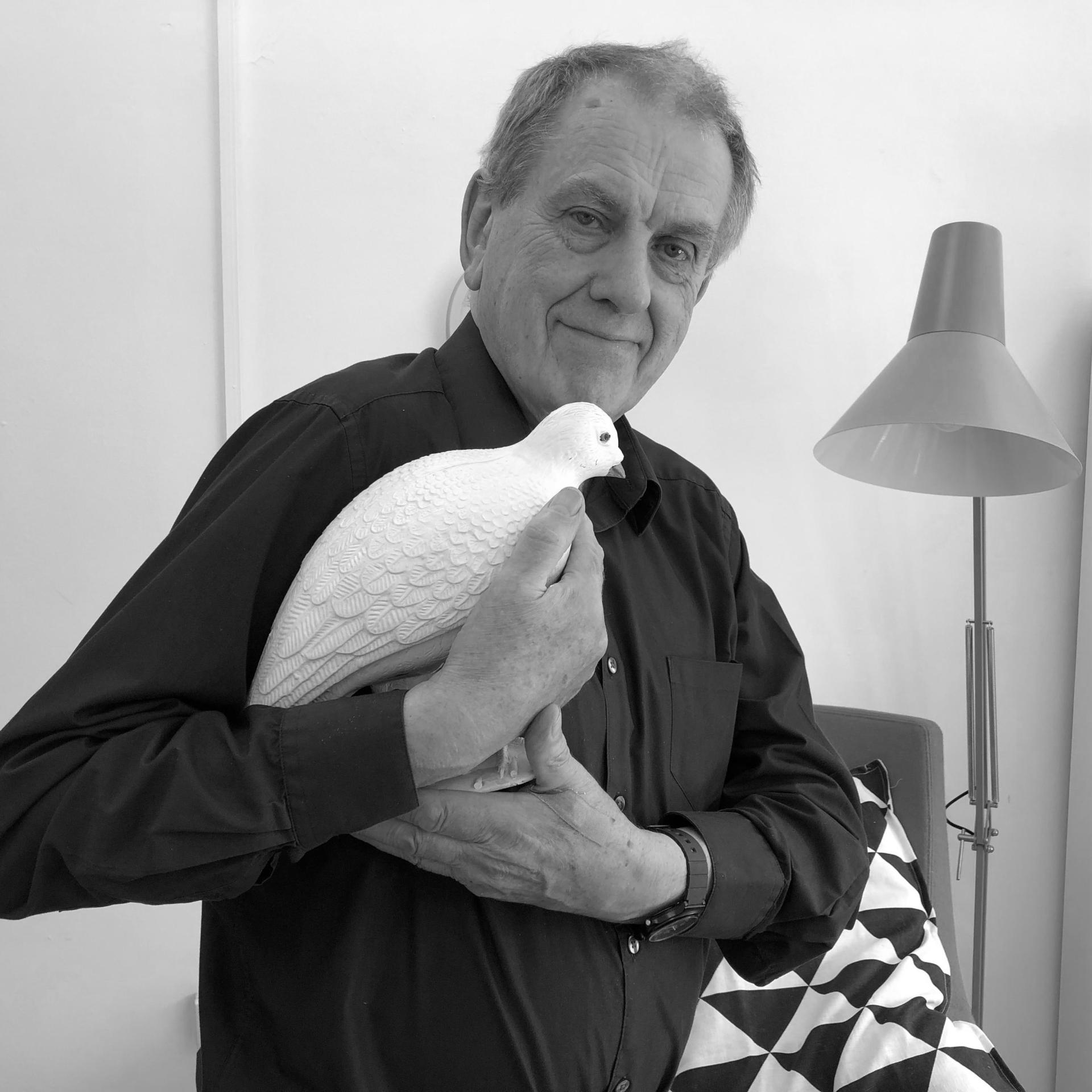 A man in a black shirt holds a white decorative bird figurine, surrounded by contemporary interior design elements.