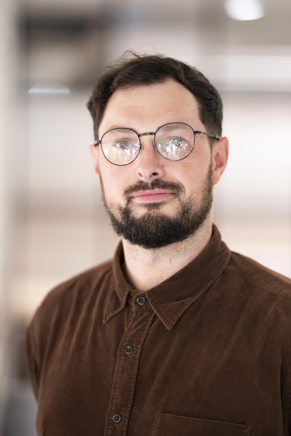 BIM manager Sam Roberts discusses digital twins' impact on achieving Net Zero targets, wearing a brown button-up shirt.