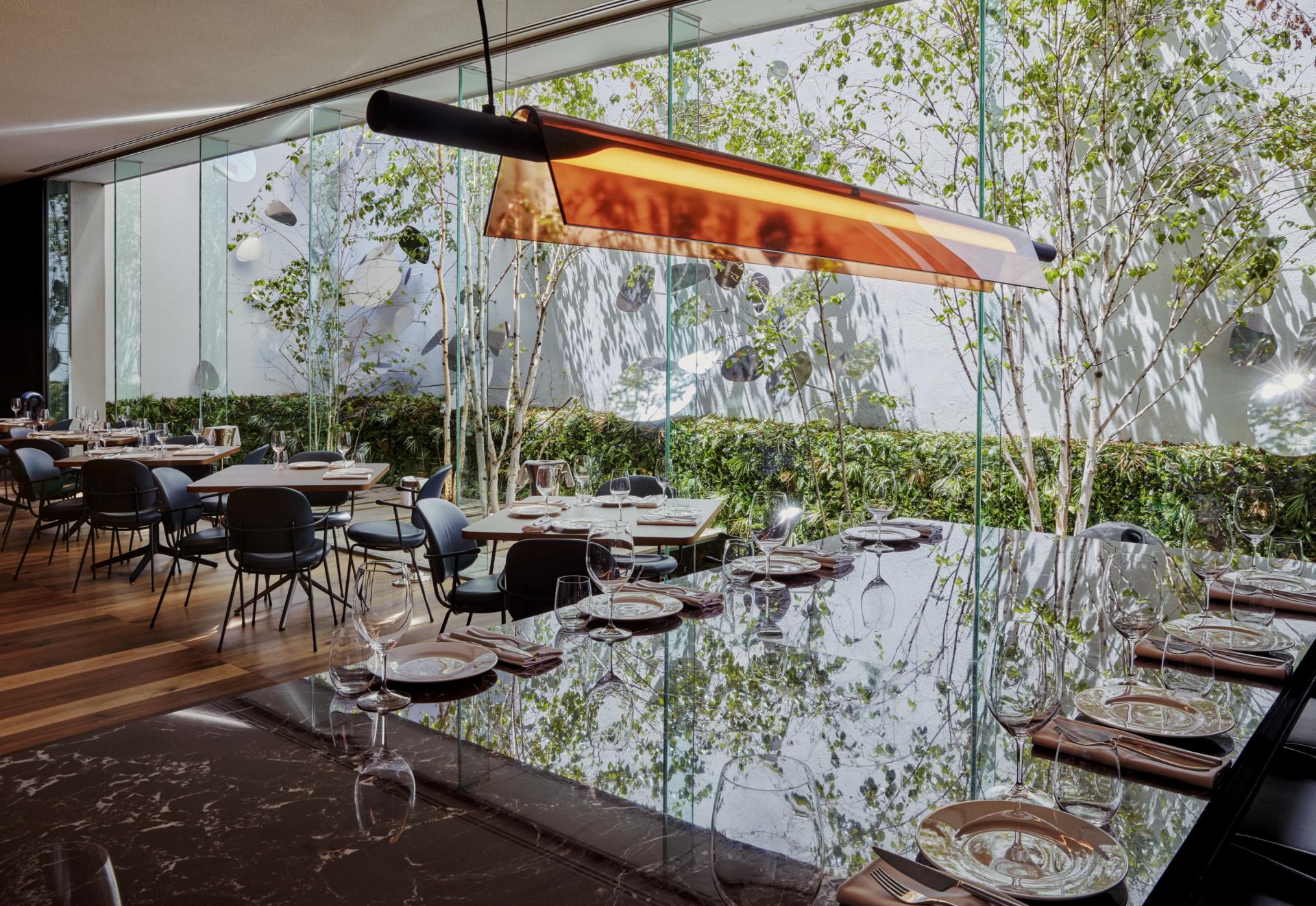 Elegant restaurant interior at Sir Victor, featuring lush greenery, modern furnishings, and a stylish reflective dining table.