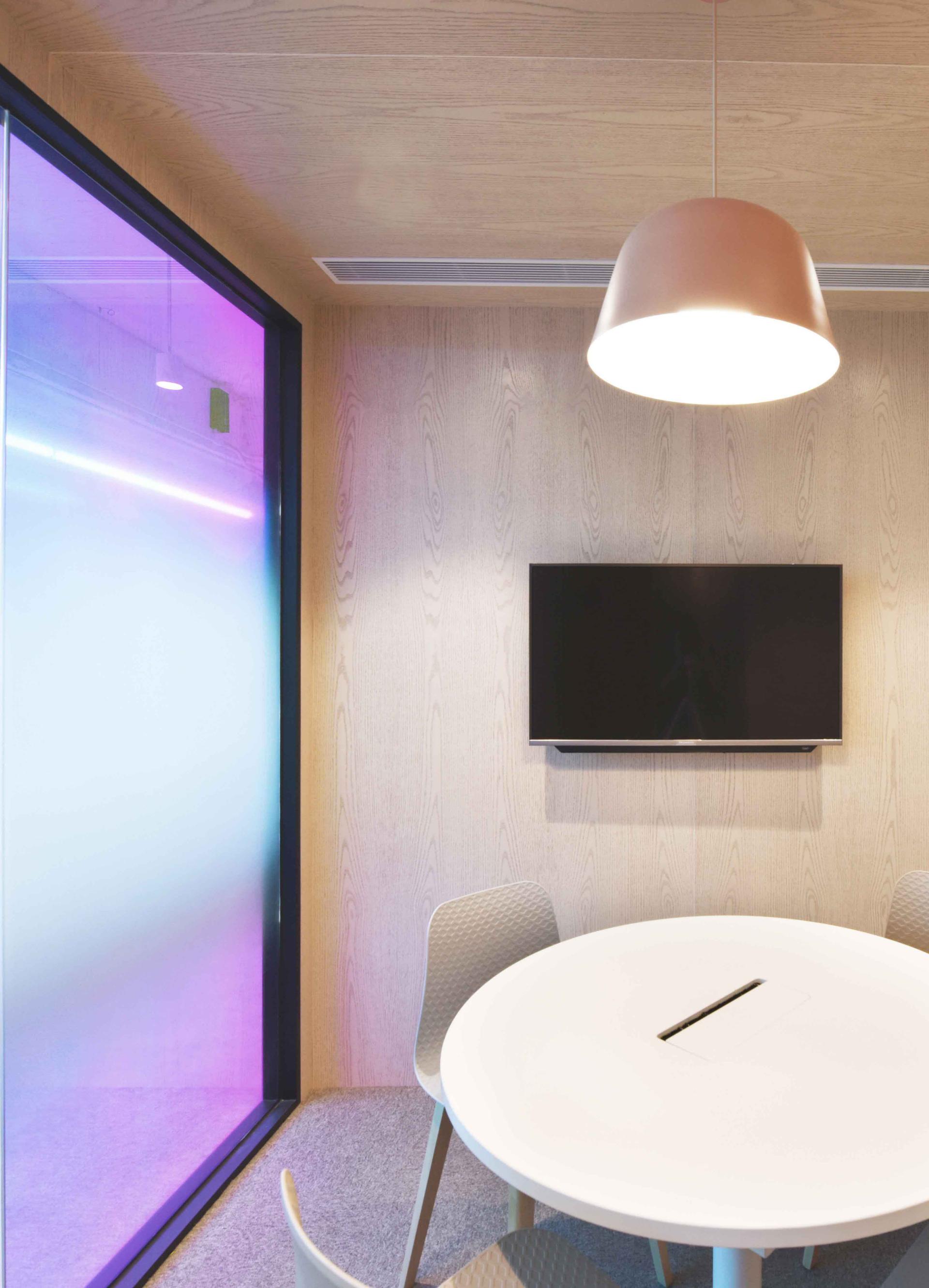 Modern conference room featuring a round table, stylish chairs, and a wall-mounted TV in a tech-focused office design.