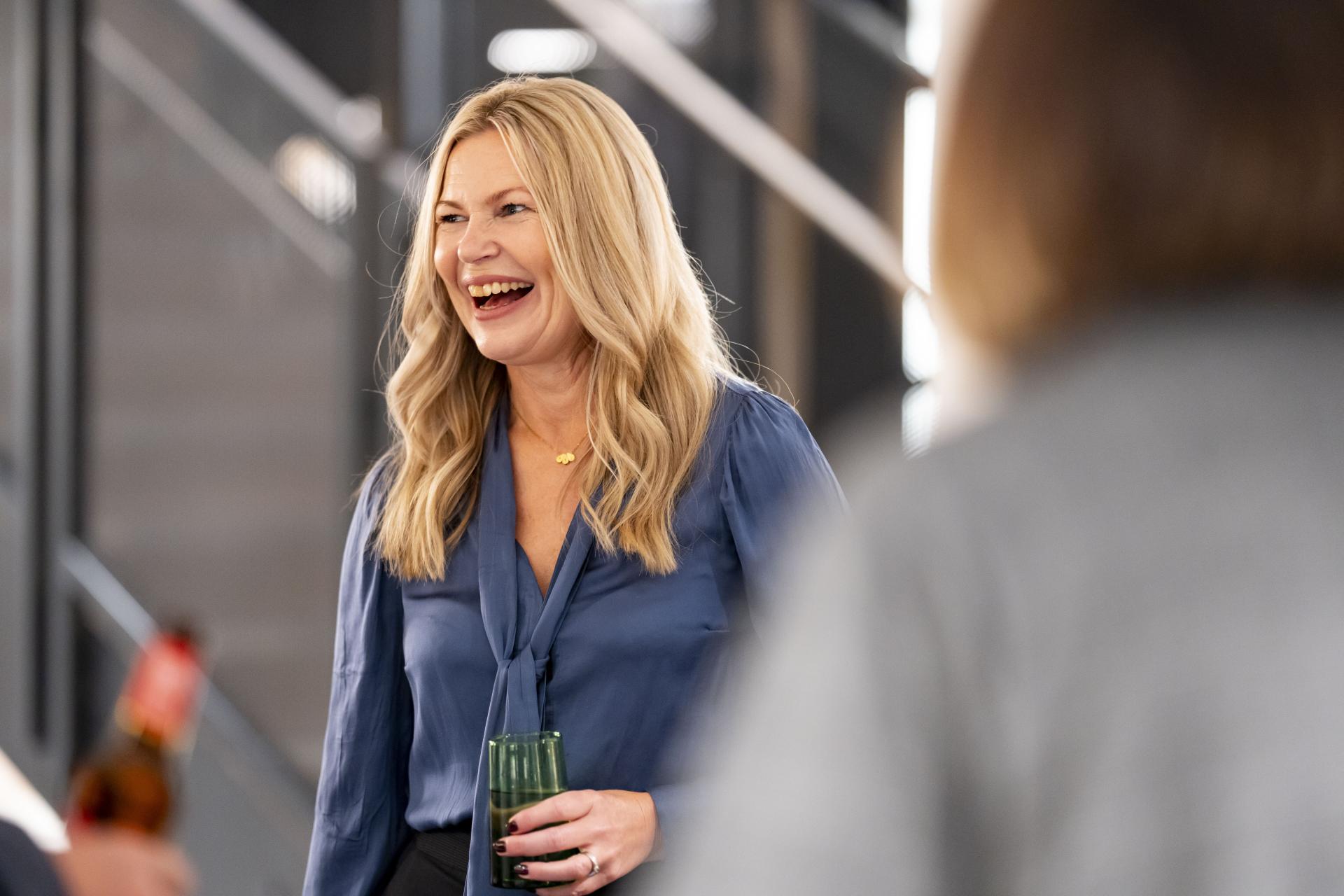 Smiling woman in a blue shirt enjoying a conversation at a modern workplace event focused on technology and data.