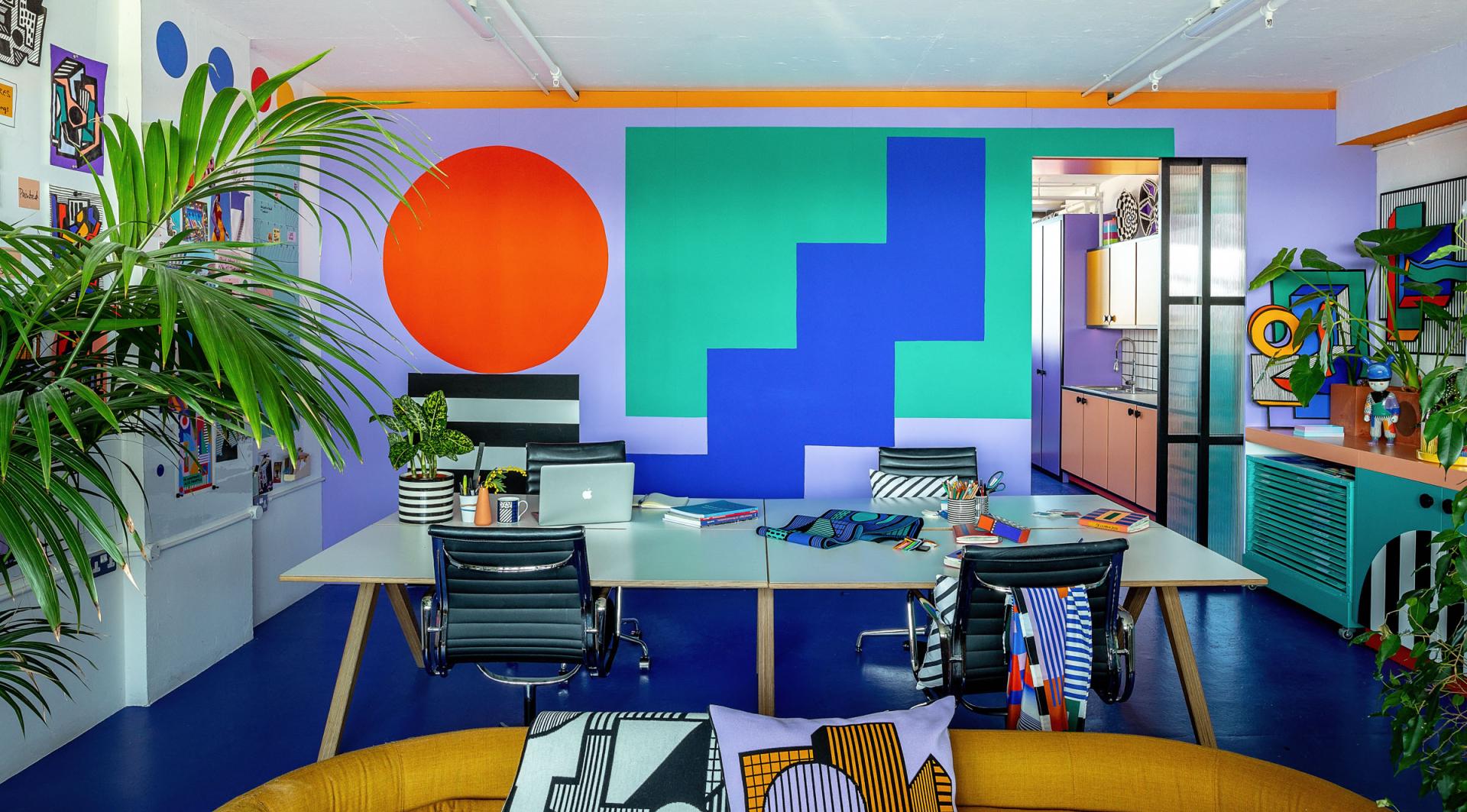 Vibrant studio workspace by Camille Walala features bold geometric murals, sleek furnishings, and decorative plants, showcasing her unique artistic style.