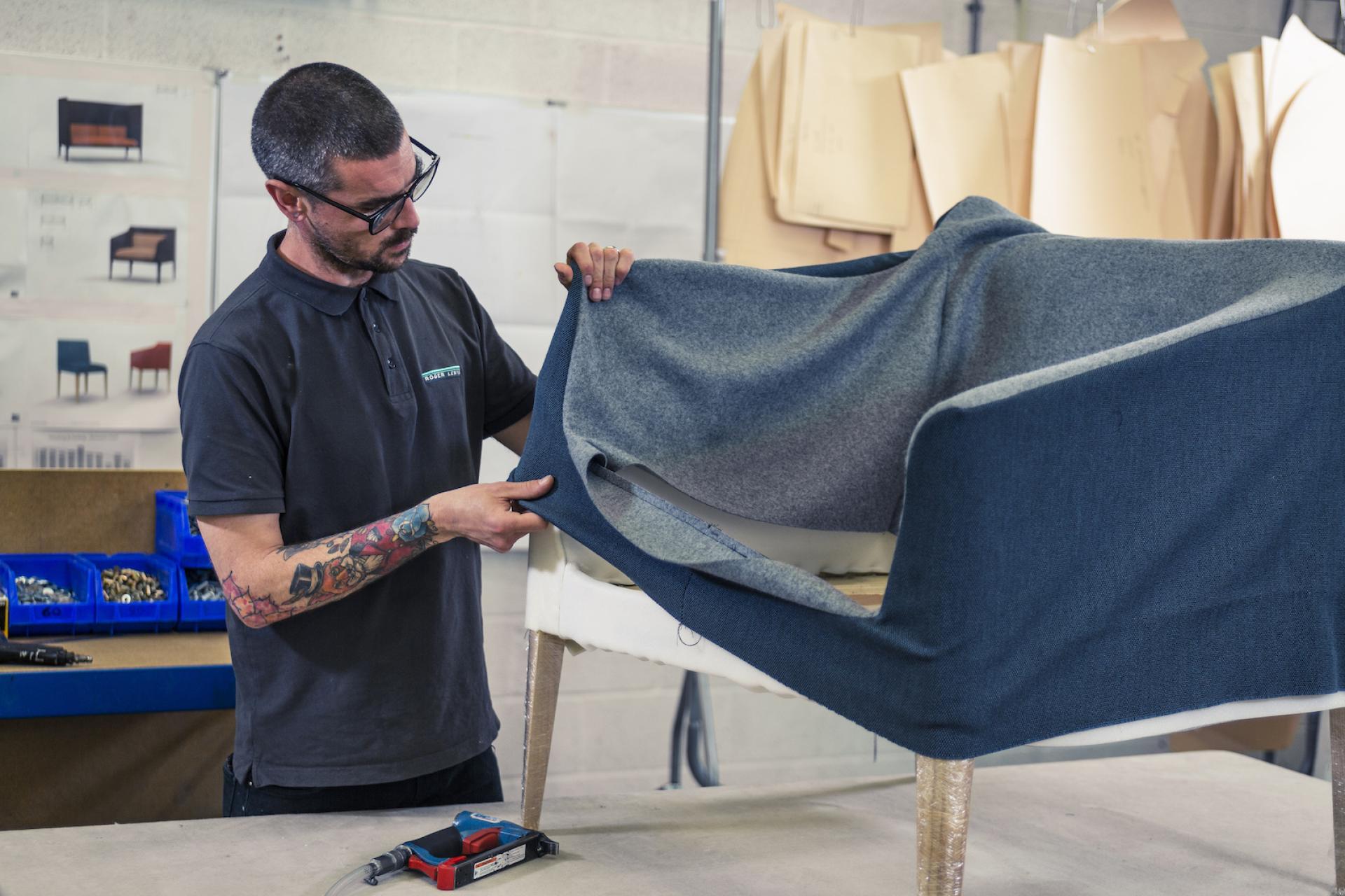 Craftsman expertly drapes fabric over a chair frame, showcasing attention to detail in furniture design by Roger Lewis.