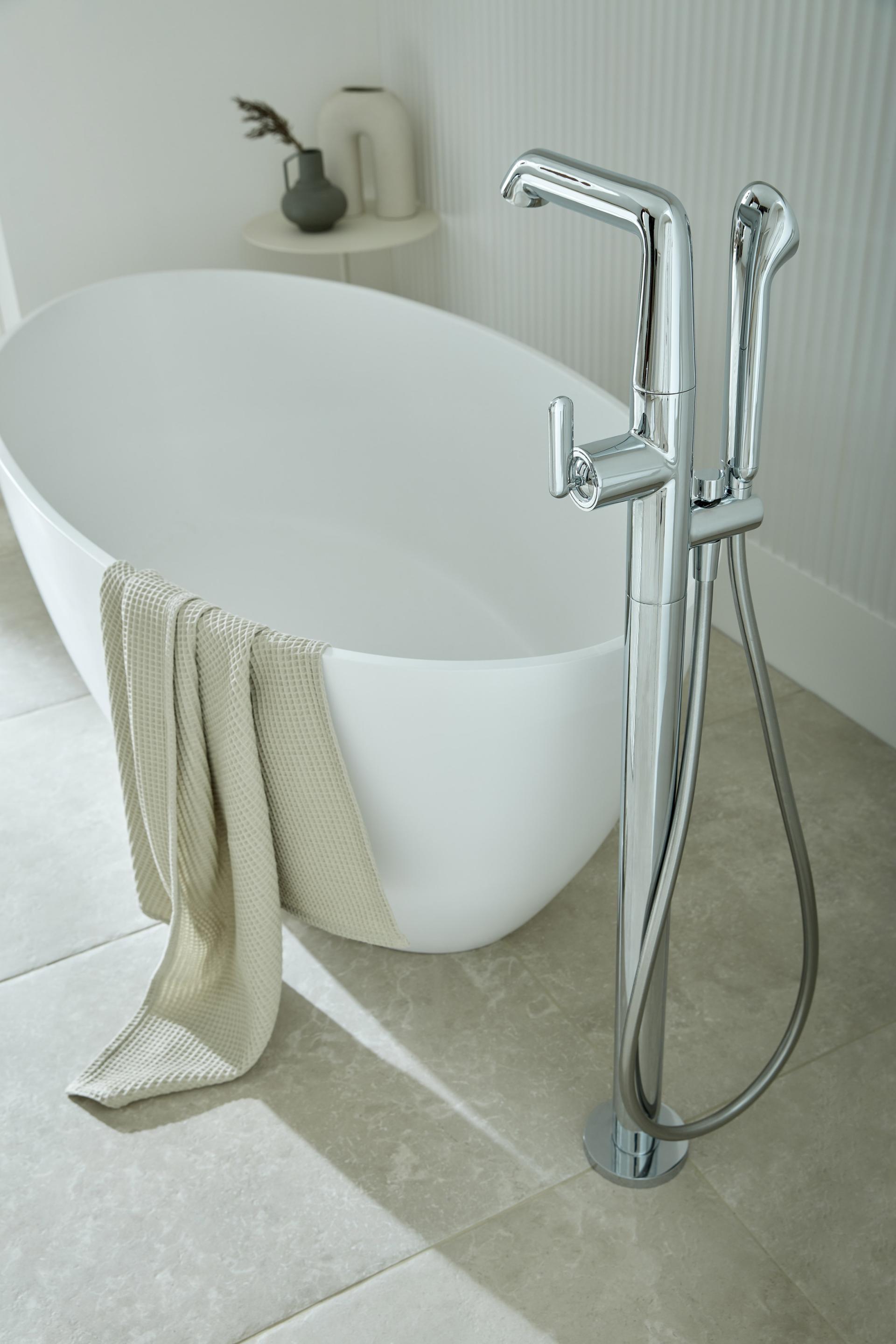 Sleek chrome freestanding bath faucet beside a stylish white bathtub, emphasizing modern design in bathroom interiors.