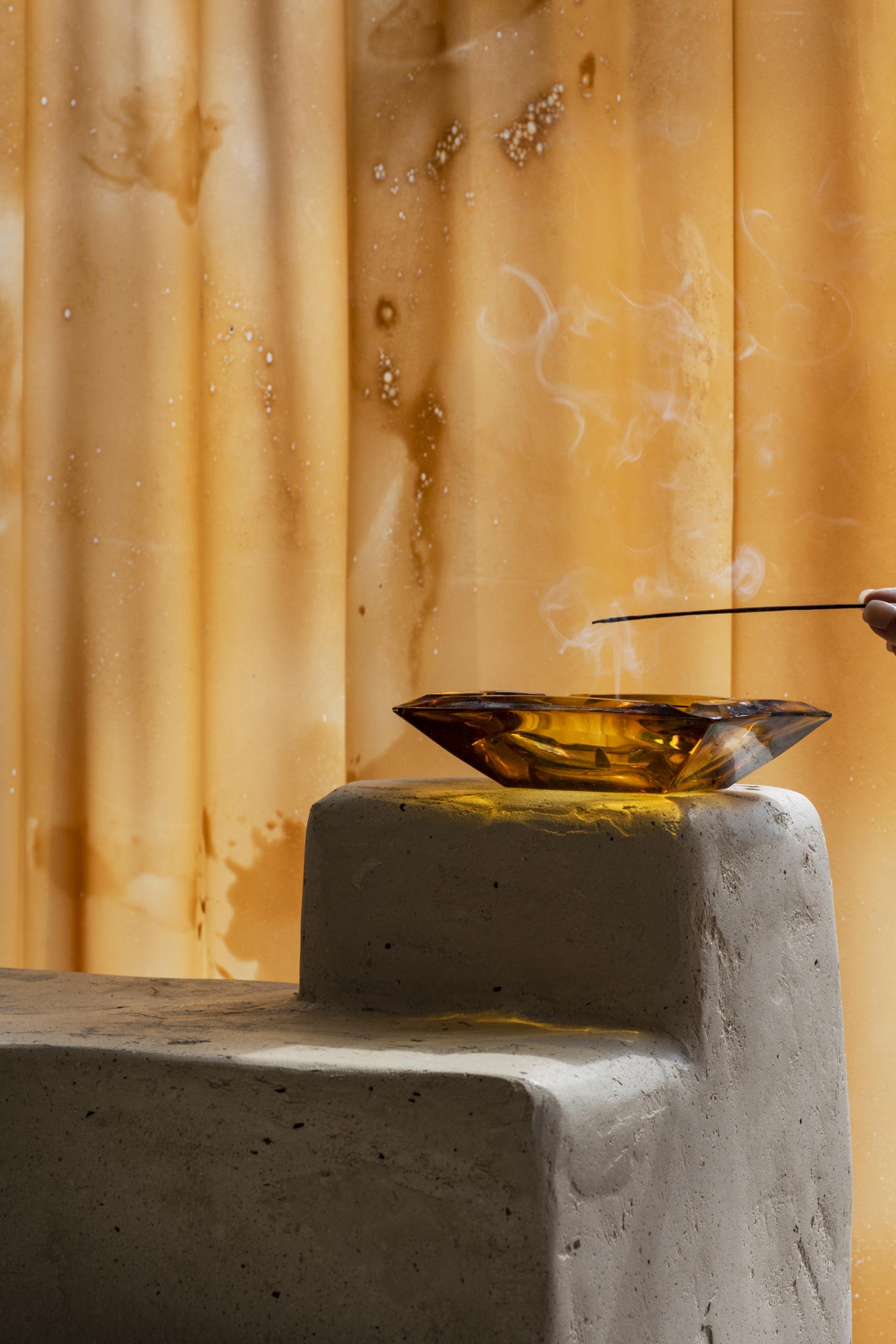 A handcrafted amber bowl rests on a modern concrete pedestal, with smoke curling gently in the air.
