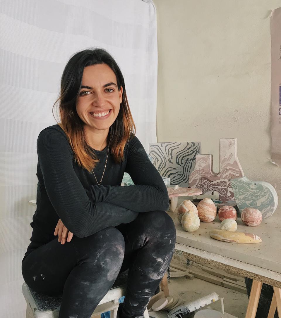 Joana Esteves smiles in her studio, surrounded by unique concrete art pieces and colorful sculptures.