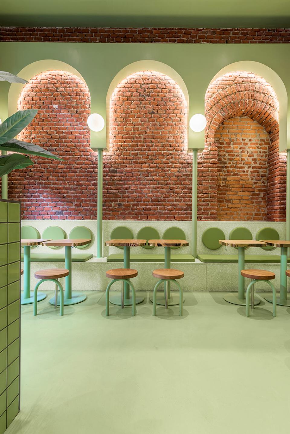 Vibrant candy-colored interior design featuring green seating, wooden tables, and brick walls at Bun restaurant in Milan.
