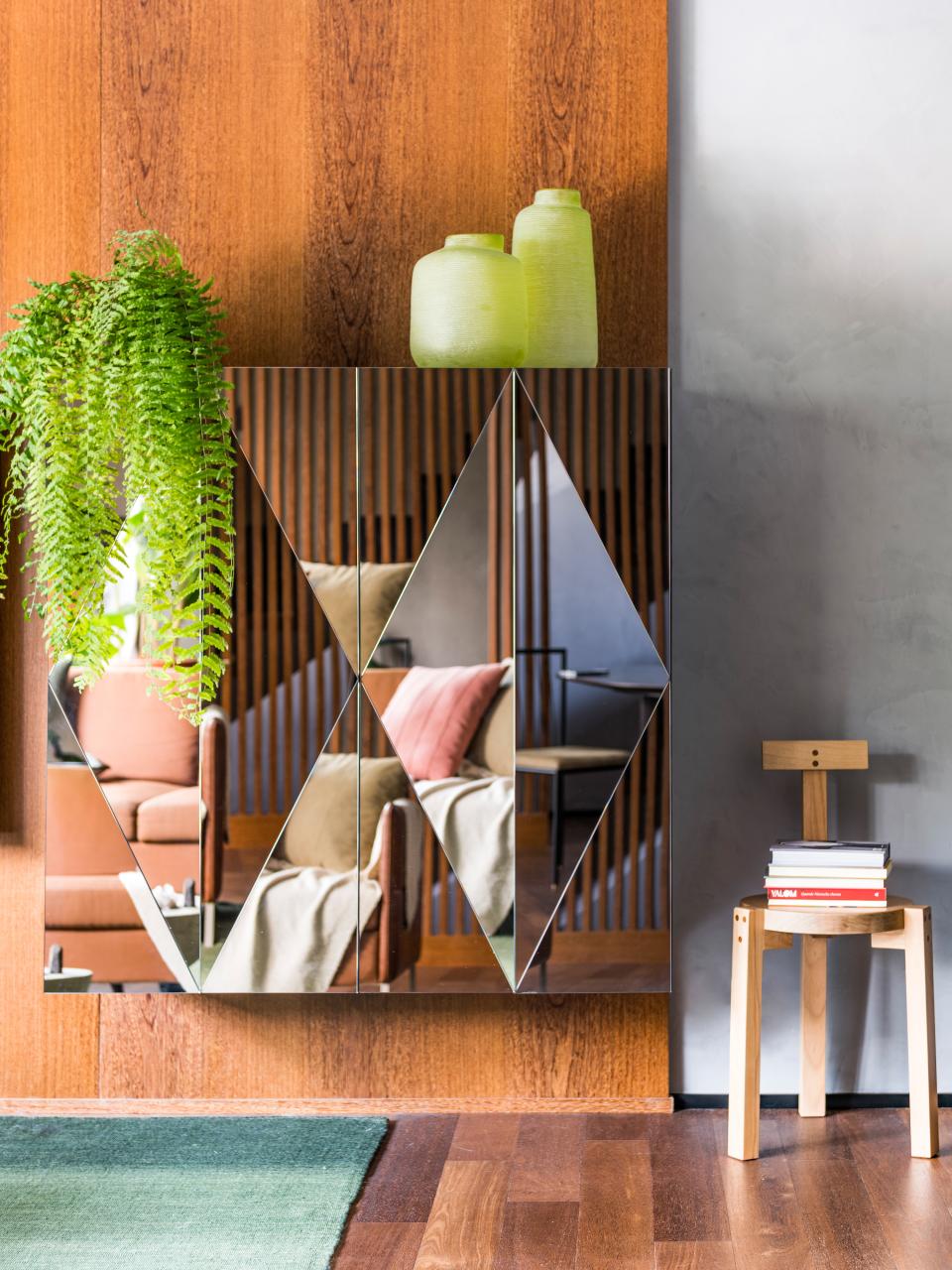 Modern interior design featuring reflective wall decor, greenery, a cozy seating area, and a minimalist wooden chair.