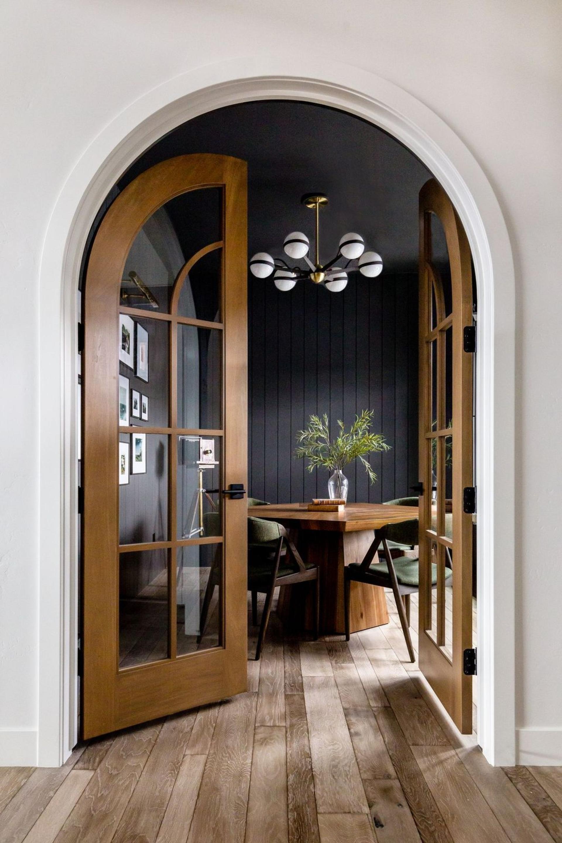 Elegant black and gold lighting fixture hangs over a stylish dining table within an archway entrance.