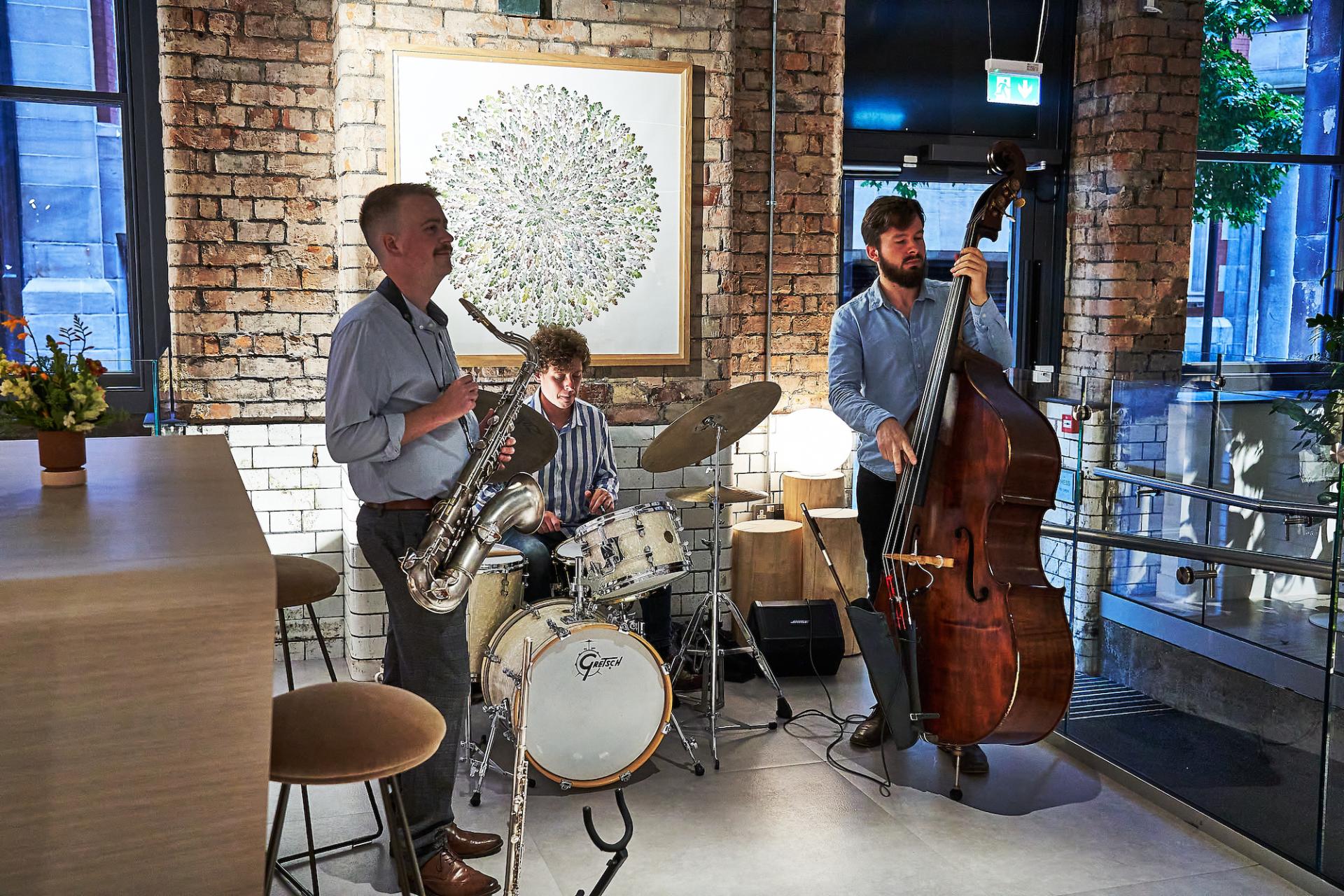 Three musicians performing live jazz, featuring a saxophonist, drummer, and double bassist in a stylish venue.
