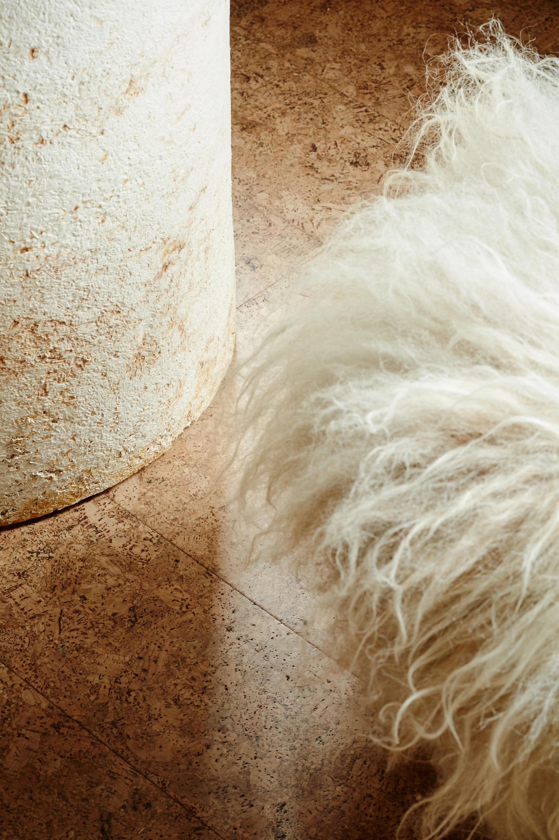 Textured cork flooring contrasting with a sculptural white element and soft, fluffy fabric, embodying sustainable design.