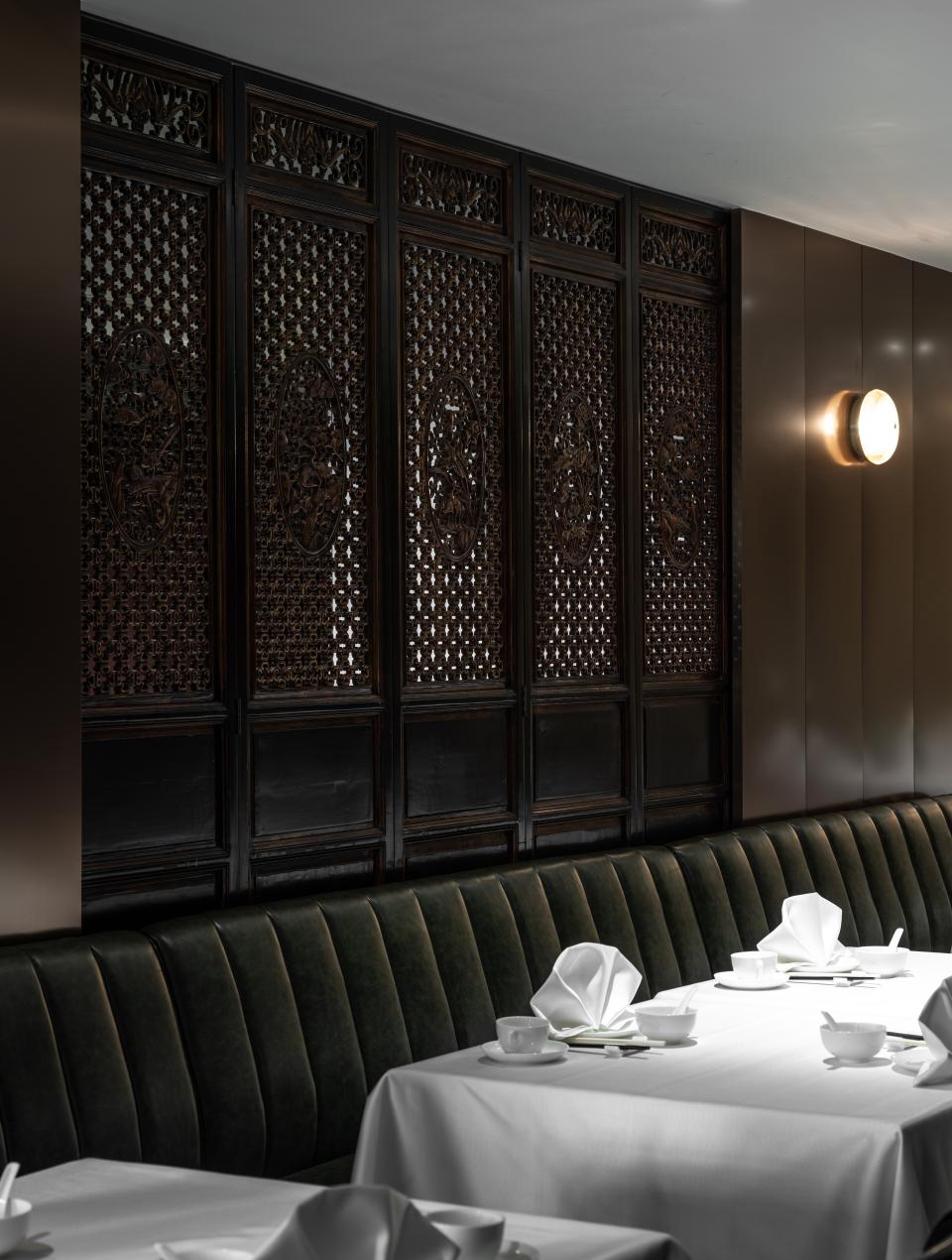 Elegant Canton Room interior featuring dark wood lattice screens, green banquette seating, and meticulously arranged dining settings.