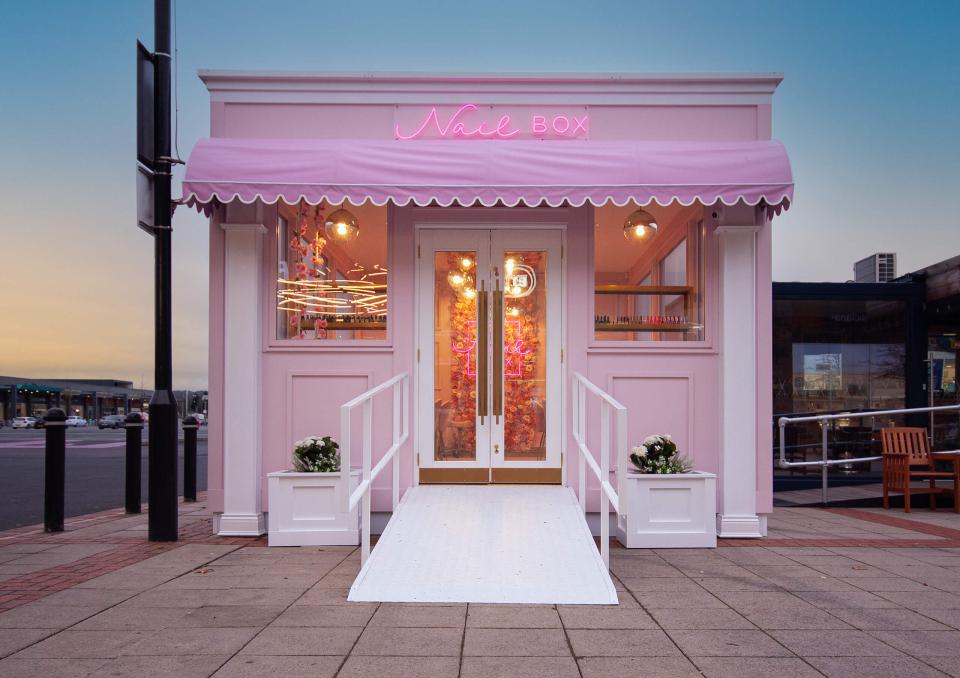 Pastel pink storefront of Nailbox, featuring a neon sign, inviting entrance, and floral decor, perfect for social media.