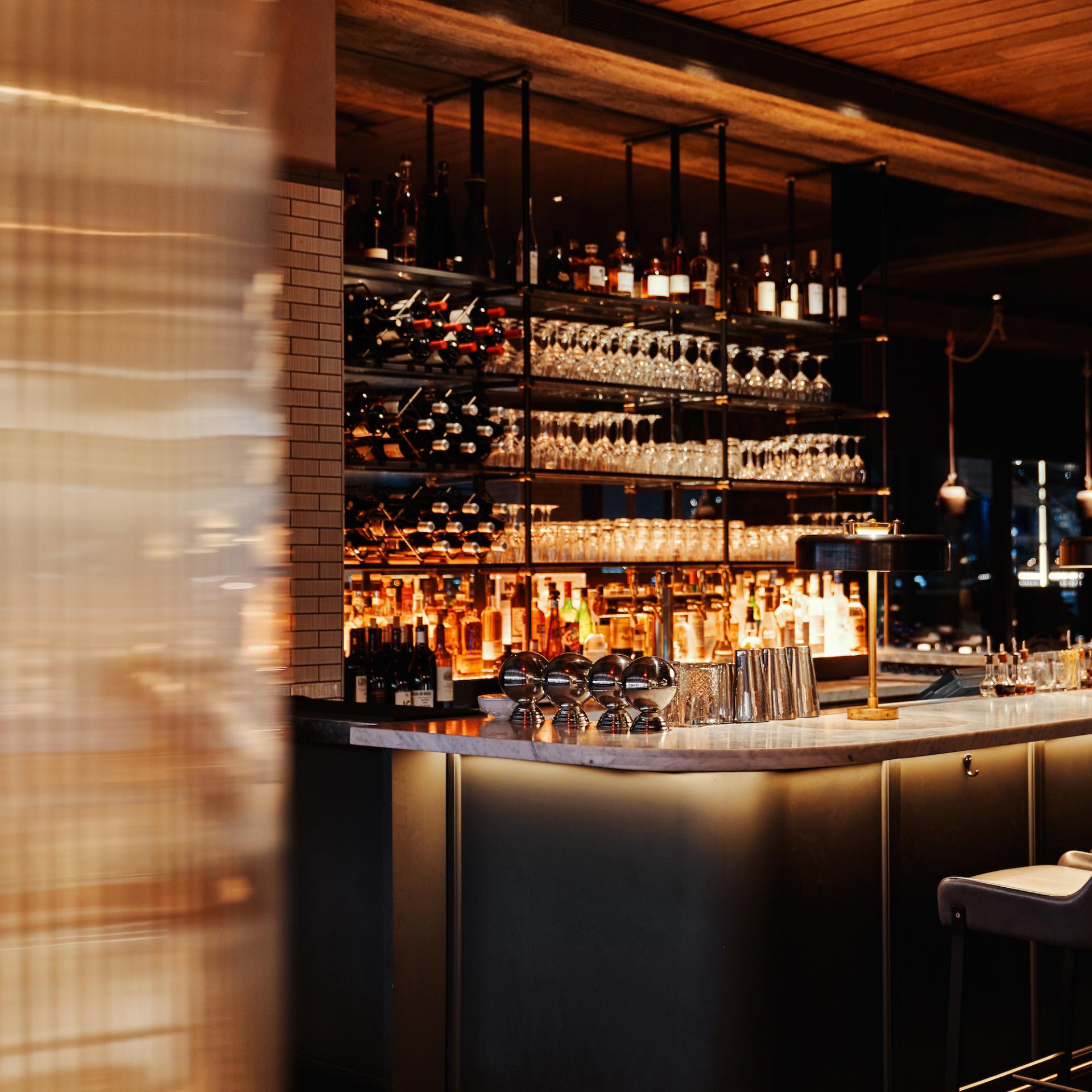 Elegant bar setup featuring shelves of wine, liquor, and glassware, reflecting Yabu Pushelberg's sophisticated interior design style.