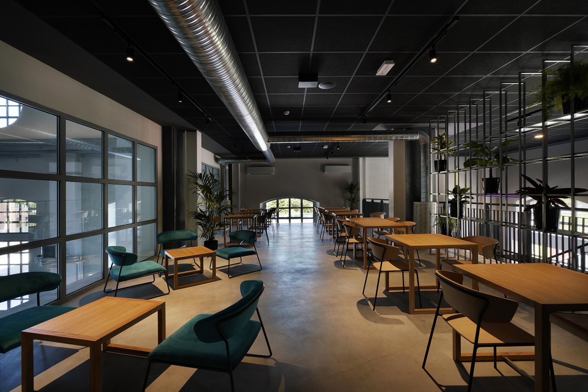 Modern interior of the Daste cultural hub in Bergamo, featuring wooden tables and green seating.