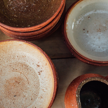Handcrafted pottery bowls and a jug display a blend of earthy tones and textures, showcasing Bruno Schooling’s artistry in ceramics.