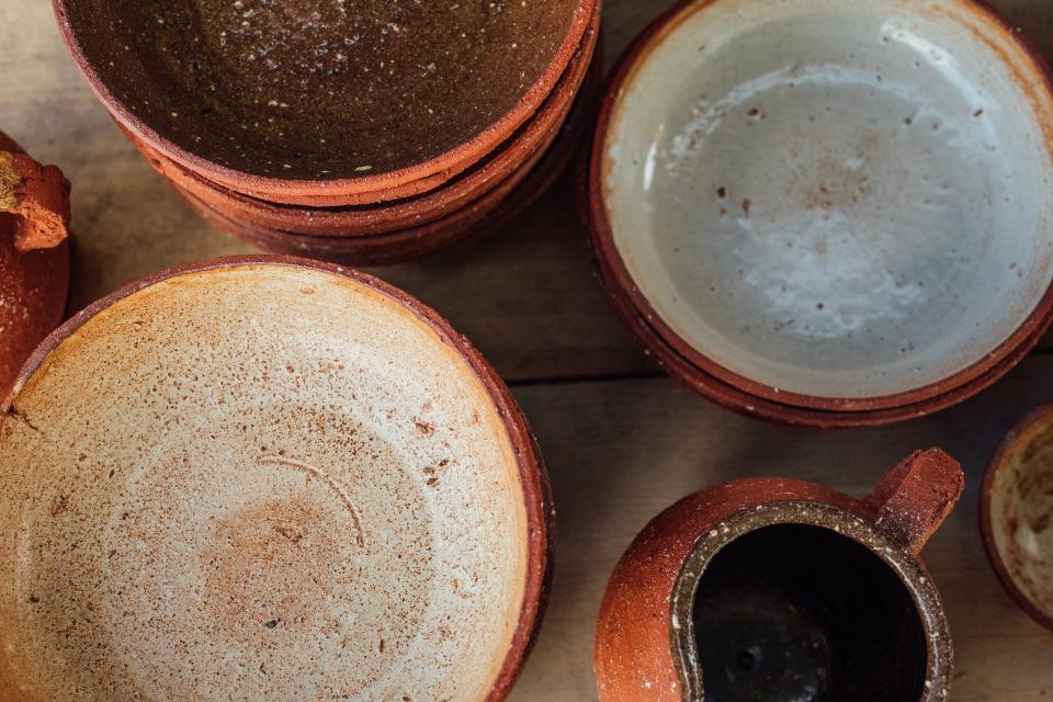 Handcrafted pottery bowls and a jug display a blend of earthy tones and textures, showcasing Bruno Schooling’s artistry in ceramics.