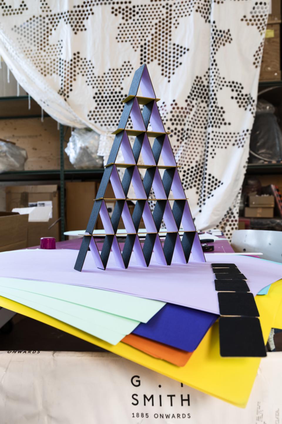 Colorful triangular paper structures arranged in a pyramid shape, with various sheets of colored paper in the foreground.