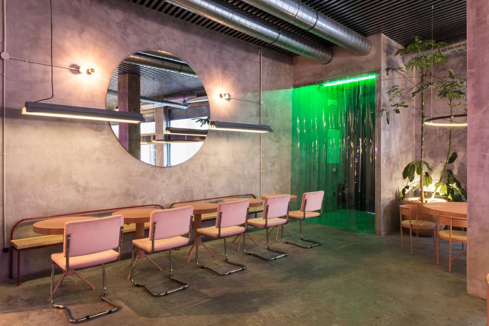 Modern restaurant interior showcasing concrete architecture, pastel furniture, and vibrant green lighting enhancing the unique design.