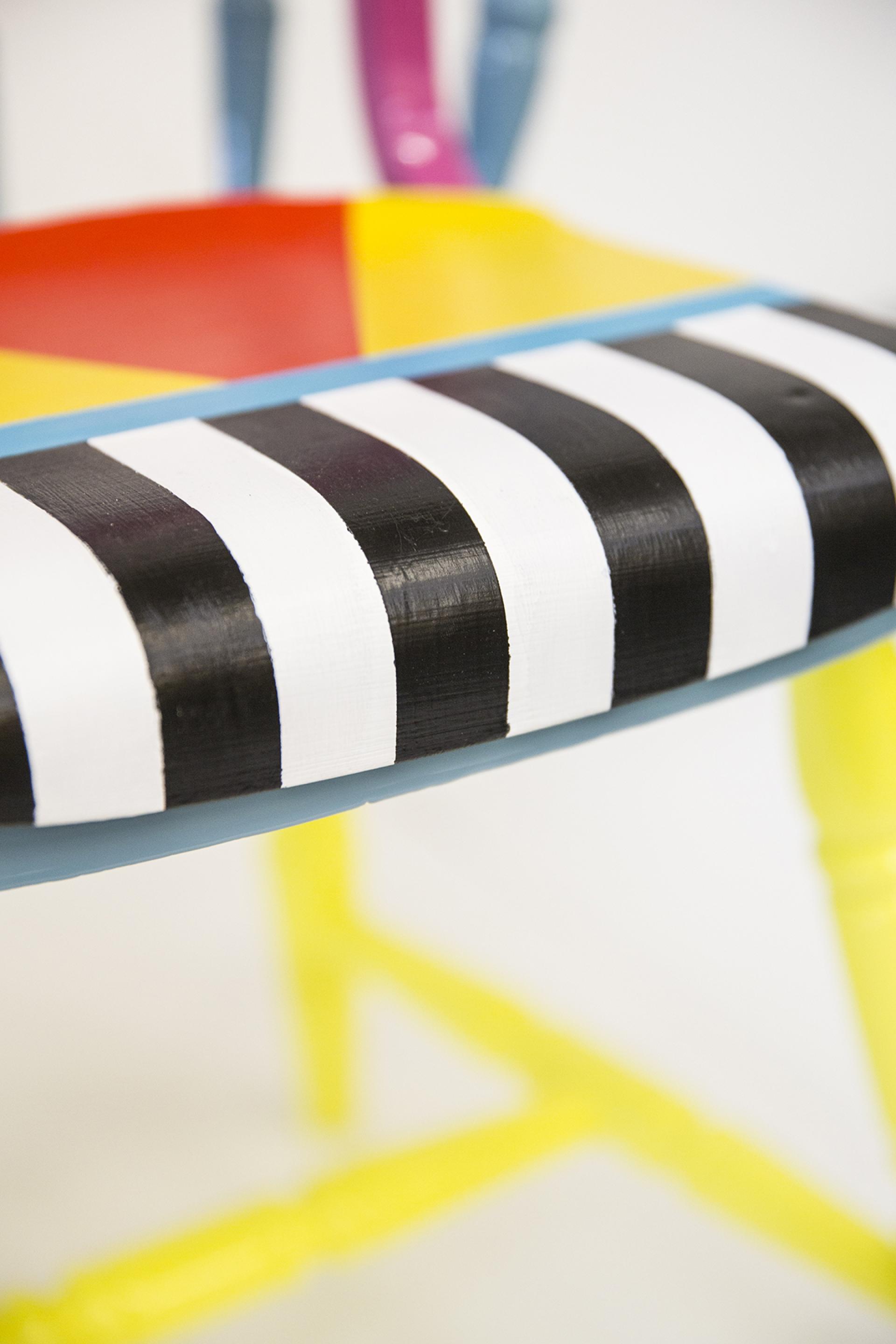 Colorful, upcycled chair with a striped seat design, showcasing Yinka Ilori's vibrant furniture style and storytelling approach.