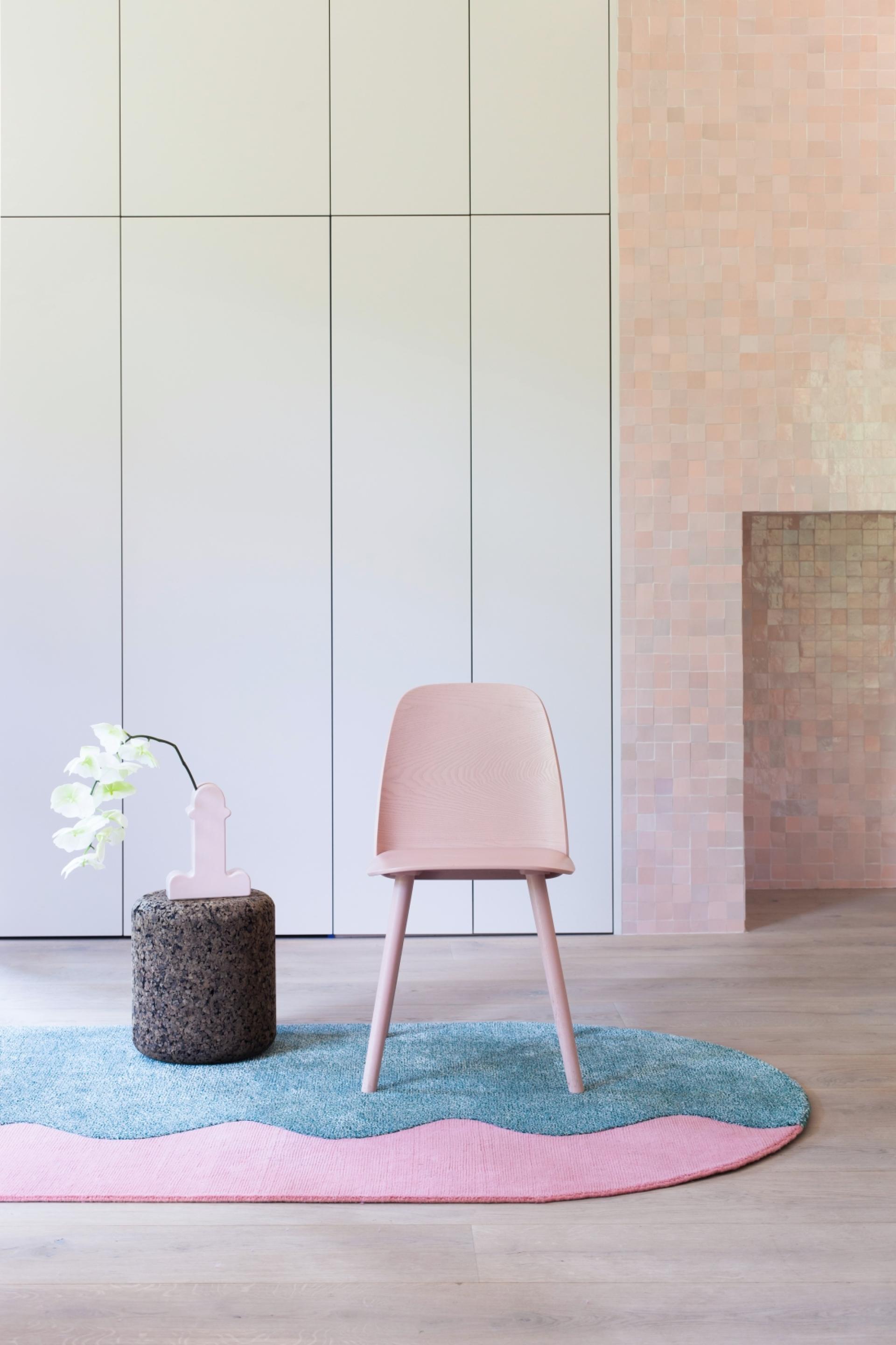 Minimalist interior featuring a pink chair, textured rug, and decorative elements, capturing contemporary design trends of 2019.