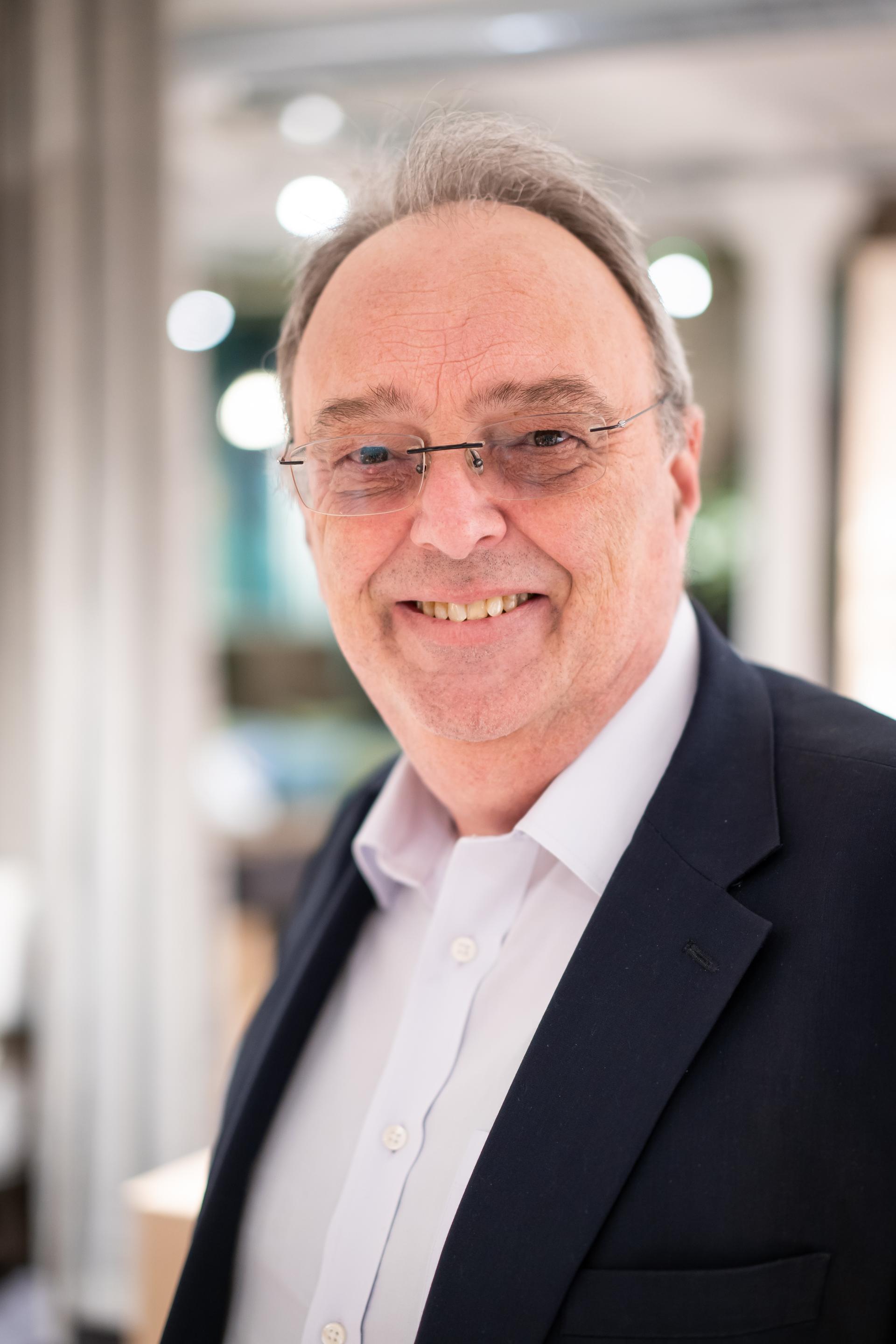 Smiling older man in a blazer, reflecting a collaborative atmosphere from a recent sustainability seminar.