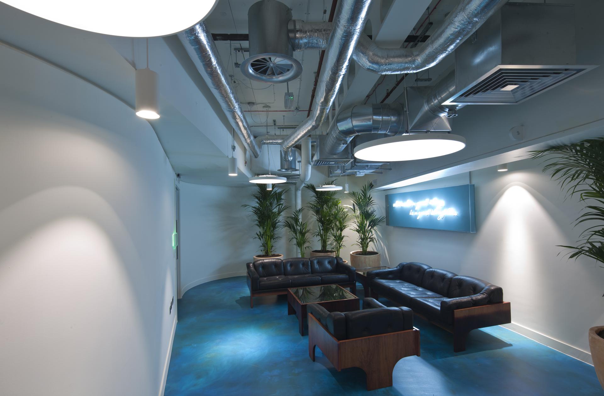 Modern interior design featuring sleek black sofas, vibrant blue flooring, and greenery, illustrating PENSON's innovative workspace aesthetic.