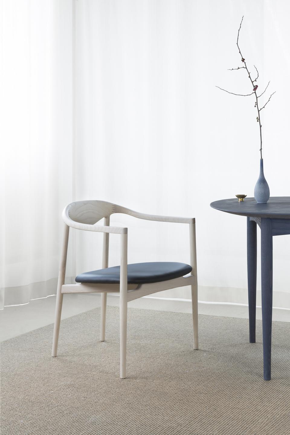 Contemporary dining chair in light wood with blue cushion, accompanied by a small round table and decorative vase.