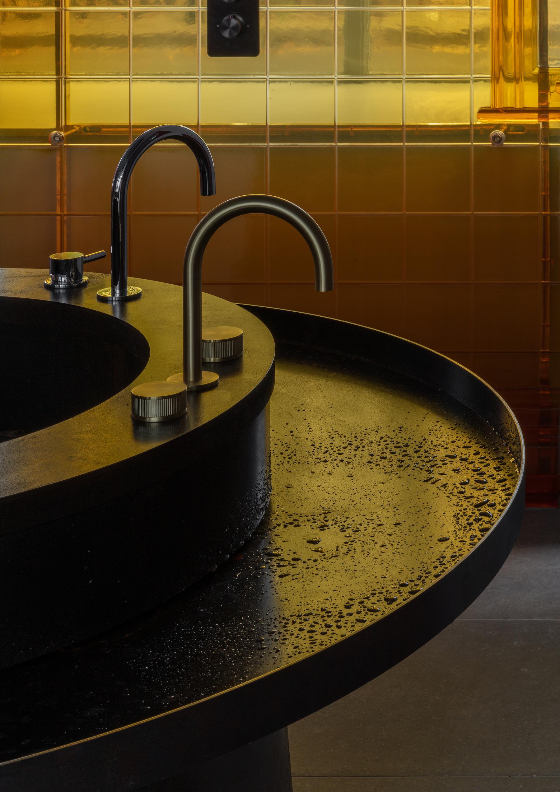 Sleek black bathroom sink with modern faucets against a warm, golden-tiled backdrop in Holloway Li's new showroom.