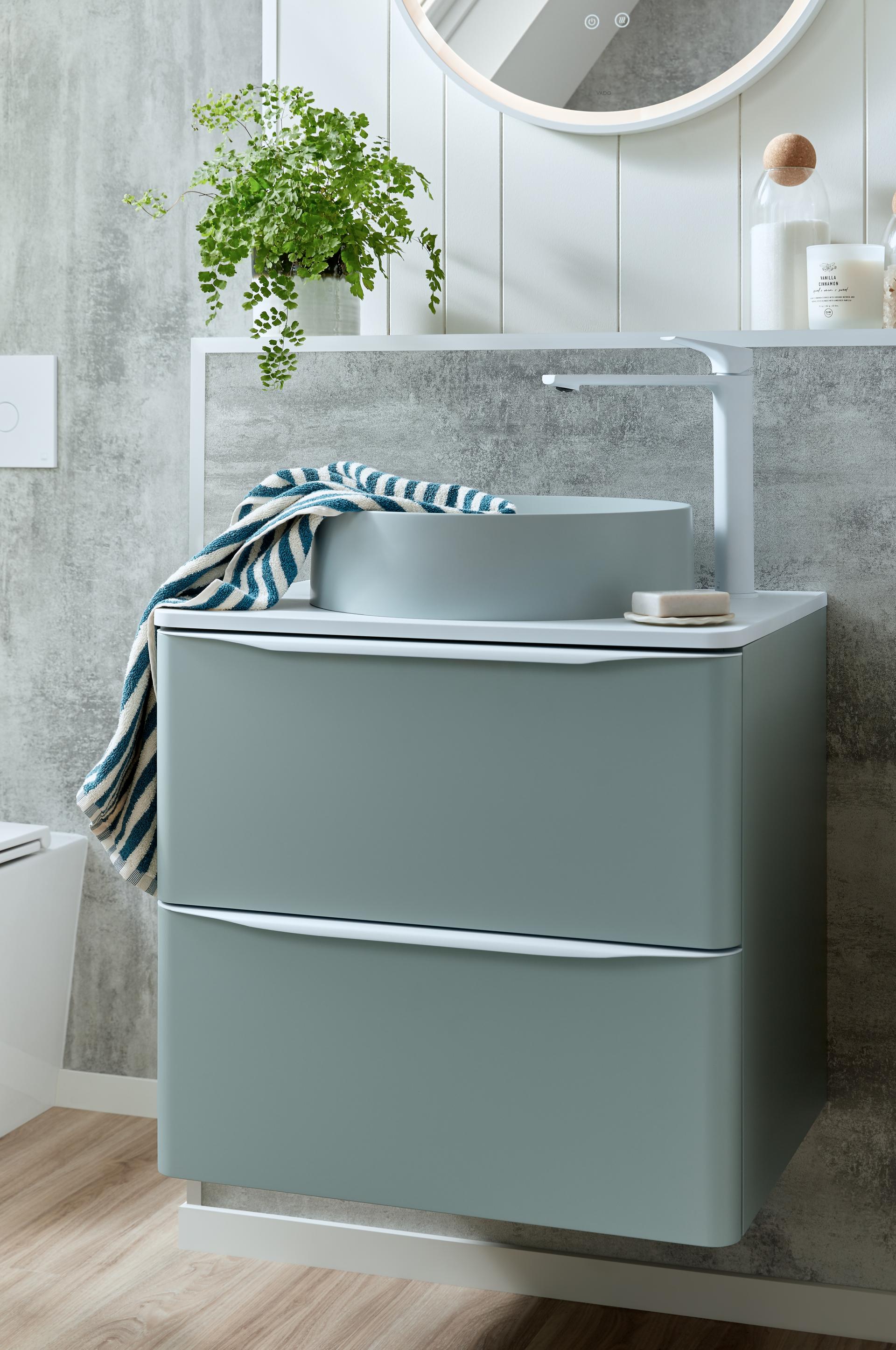 Stylish VADO bathroom sink with a modern grey cabinet, decorative plant, and striped towel, highlighting contemporary design.