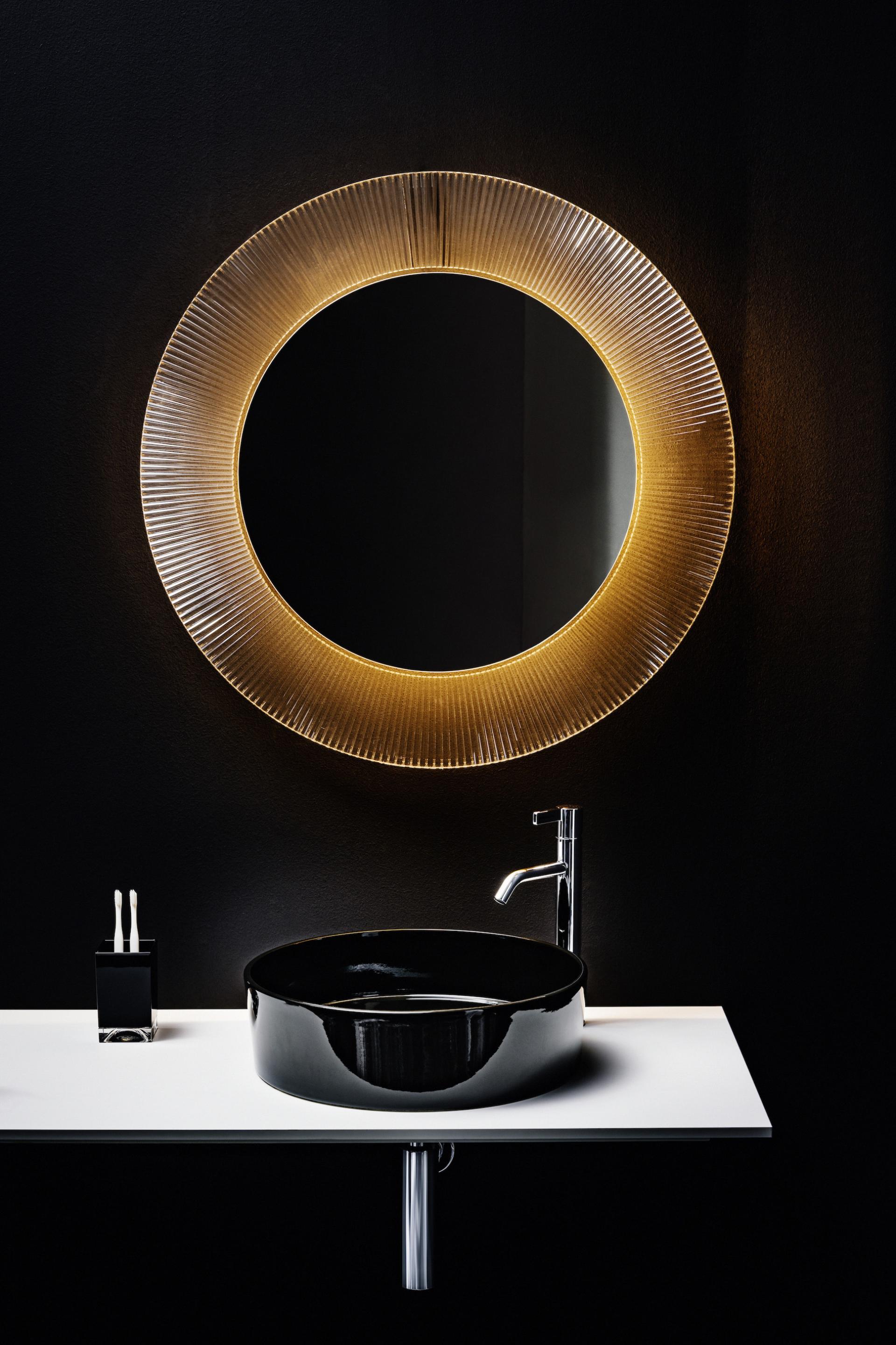 Stylish bathroom featuring a sleek black basin, contemporary faucet, and an illuminated circular mirror against a dark wall.