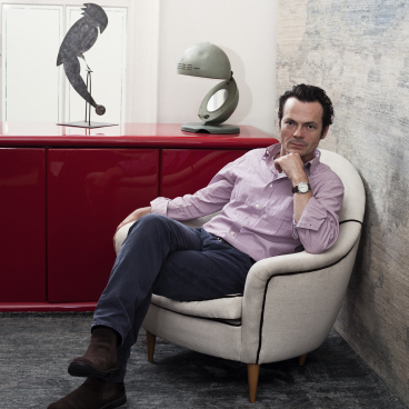 Luke Irwin sitting thoughtfully in a stylish armchair, surrounded by contemporary decor and a luxurious rug design.