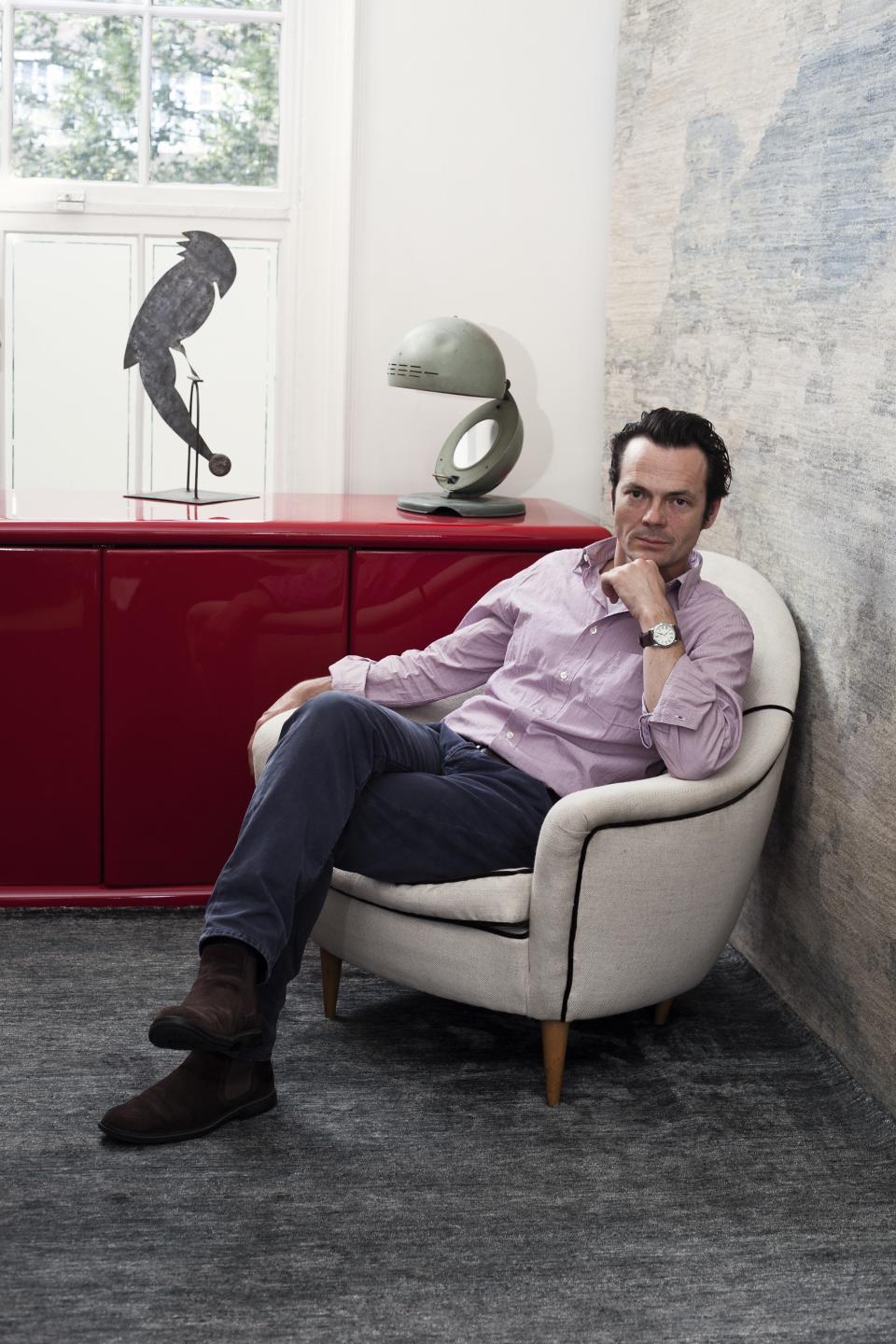 Luke Irwin sitting thoughtfully in a stylish armchair, surrounded by contemporary decor and a luxurious rug design.