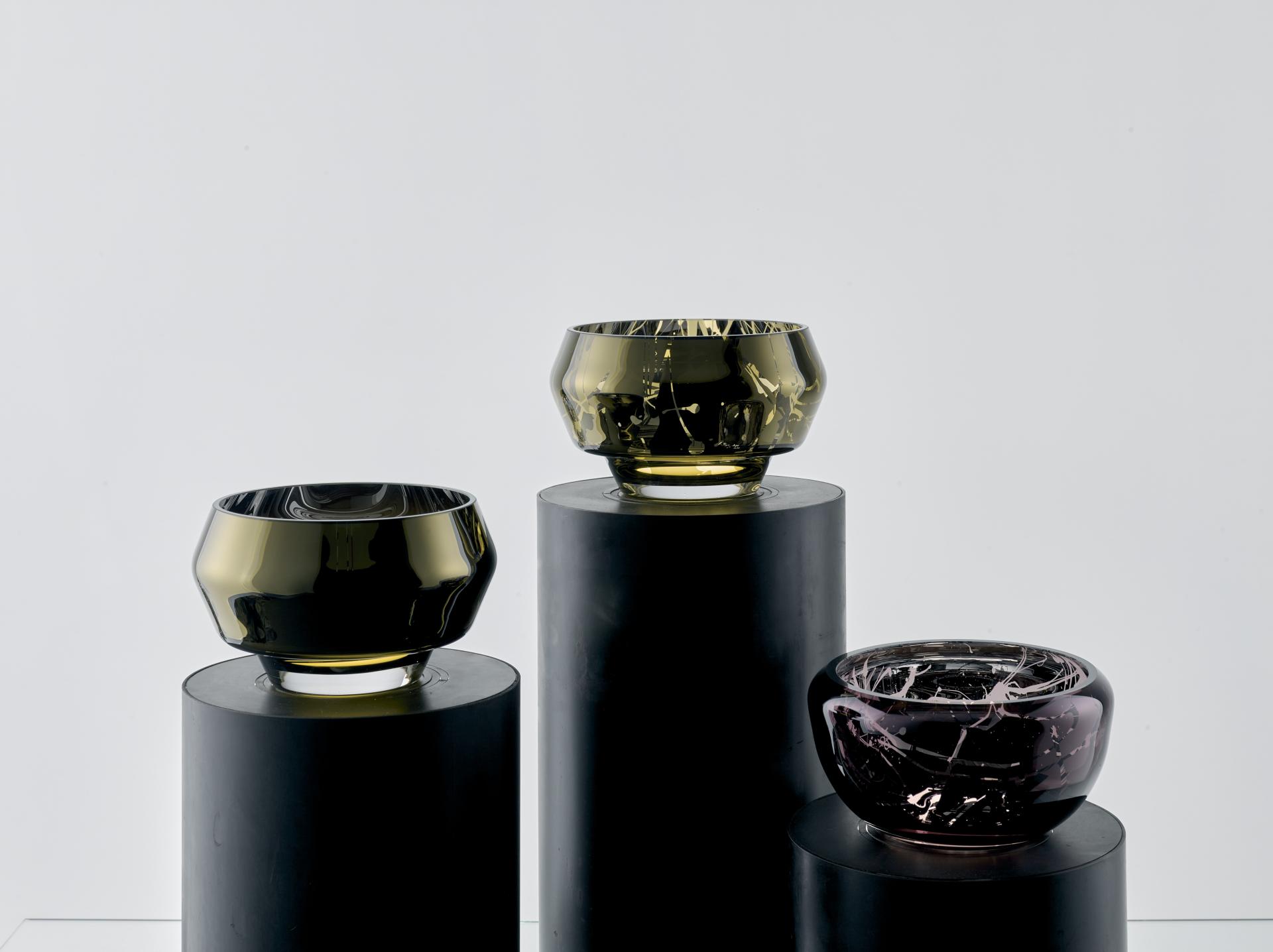 Elegant glass bowls in various colors displayed on black pedestals, showcasing innovative Baltic craftsmanship and design.