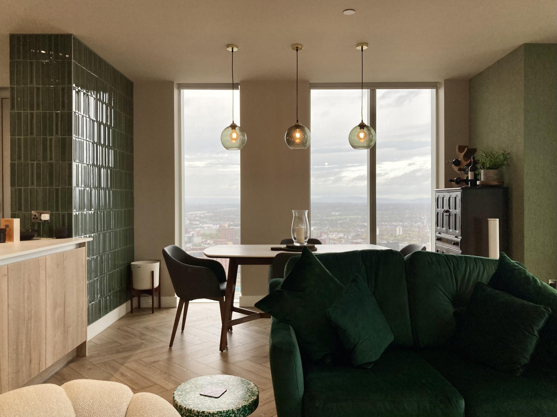 Modern interior of a Manchester design studio featuring a green accent wall, stylish furniture, and large windows with city views.