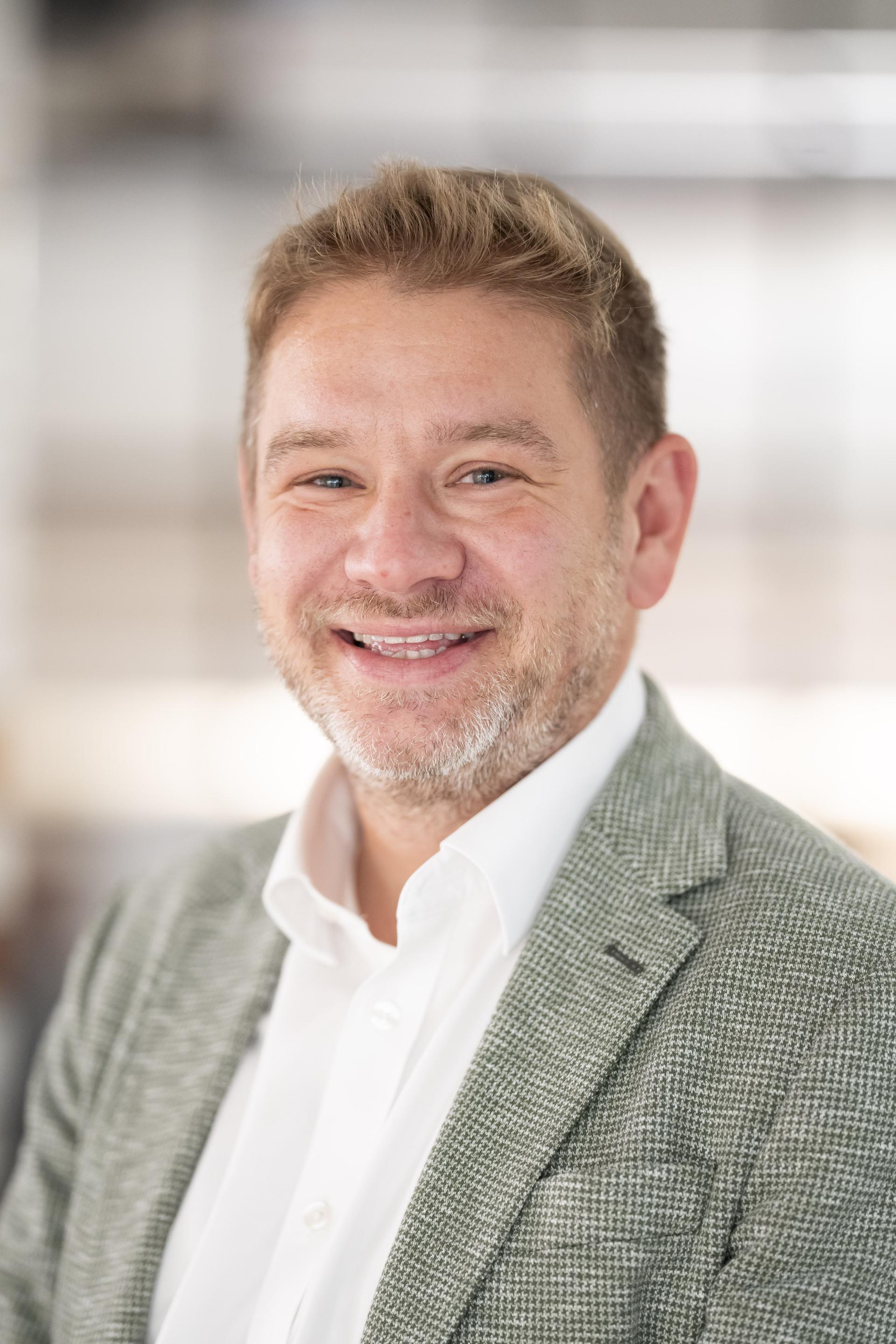 Professional man smiling in a modern office setting, reflecting the impact of data on workplace dynamics and technology.