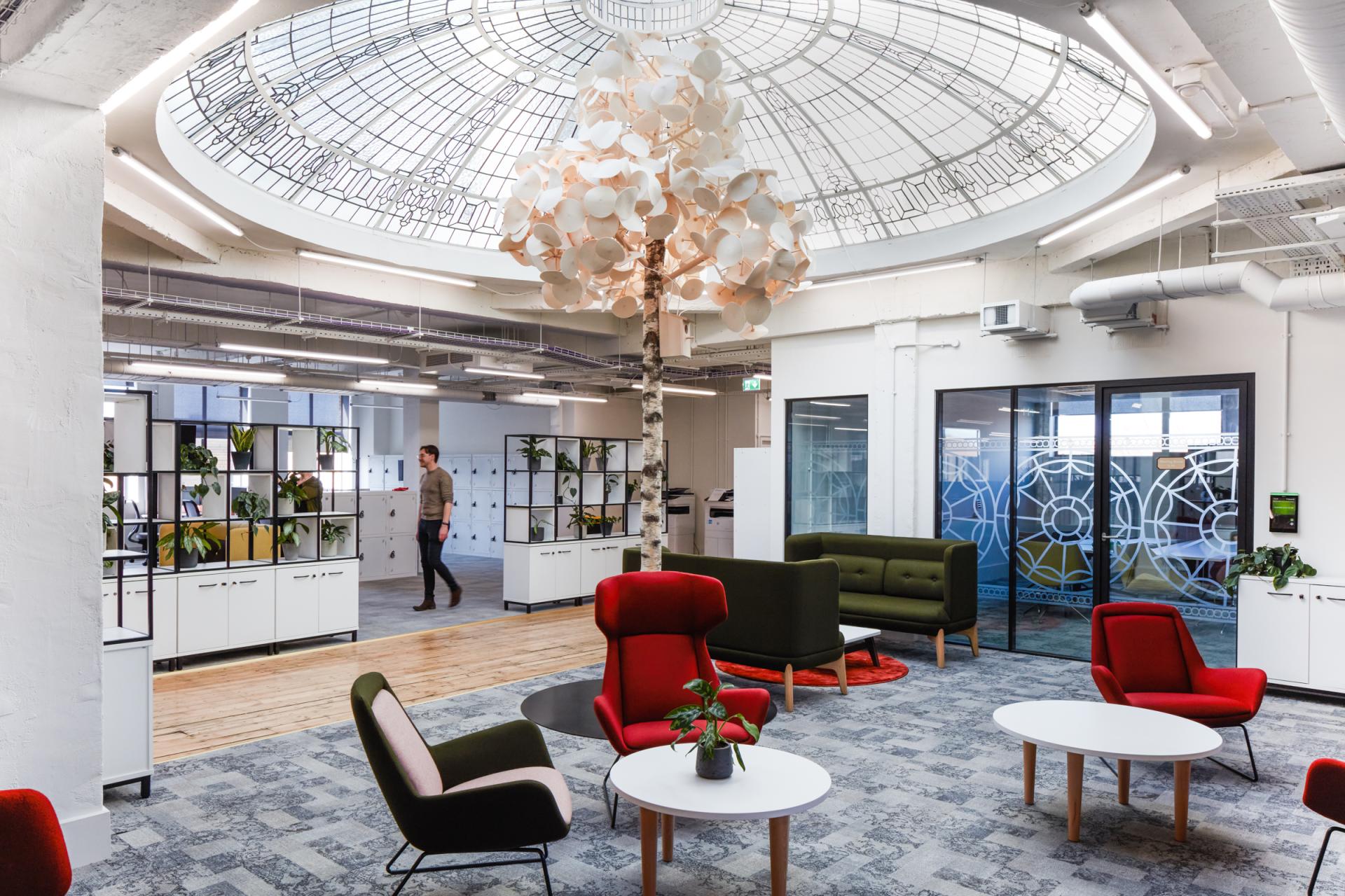 Modern workspace featuring vibrant seating, greenery, and a large skylight, emphasizing innovative design for future work environments.