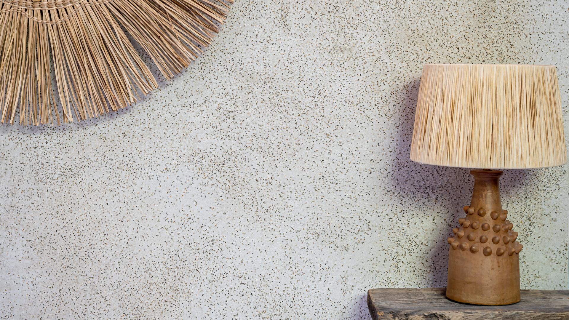 Natural textured wall with a statement lamp featuring a straw shade and unique ceramic base, showcasing surface design trends.