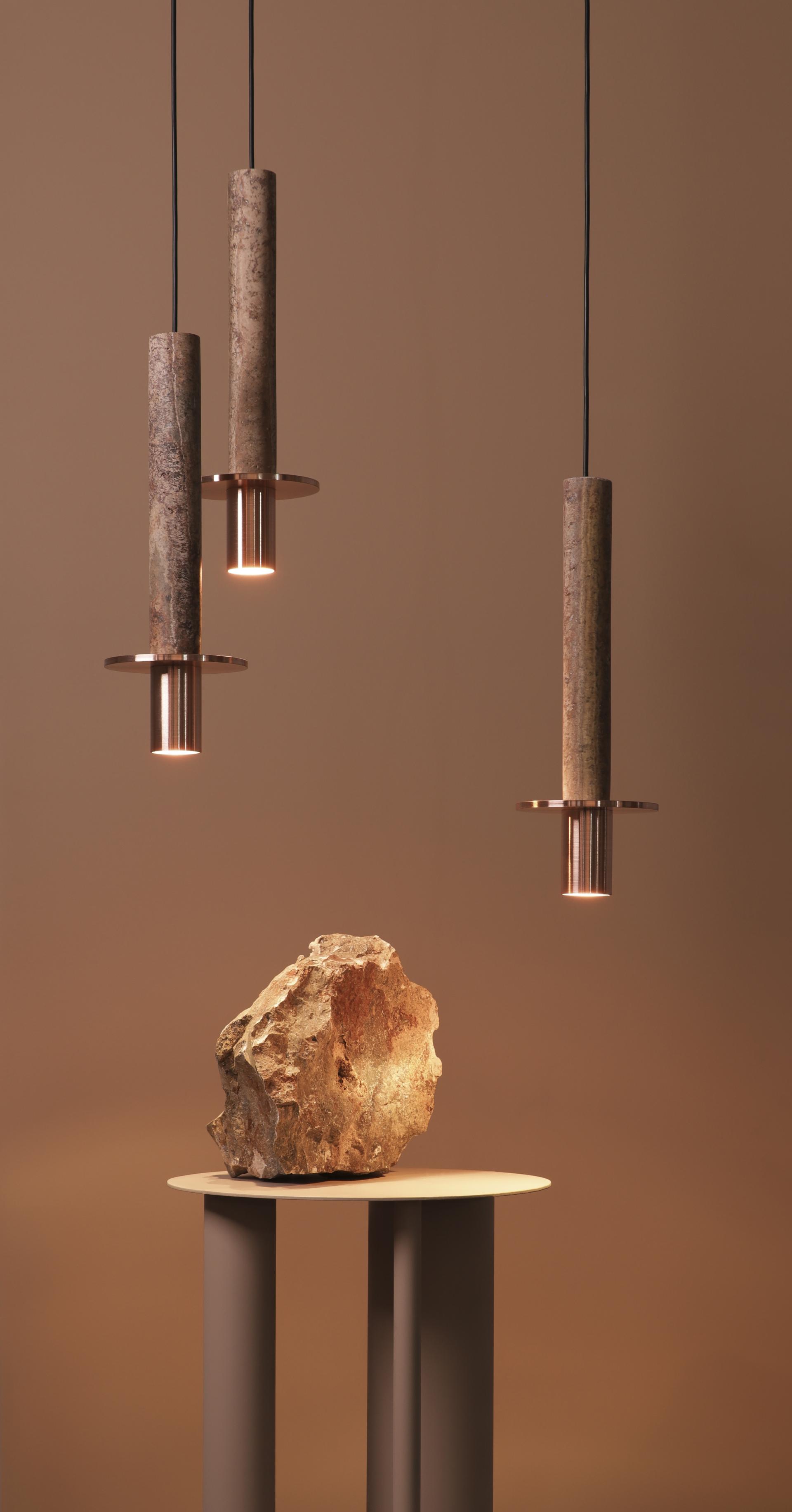 Three pendant lamps with textured finishes hang above a natural stone display on a modern pedestal.