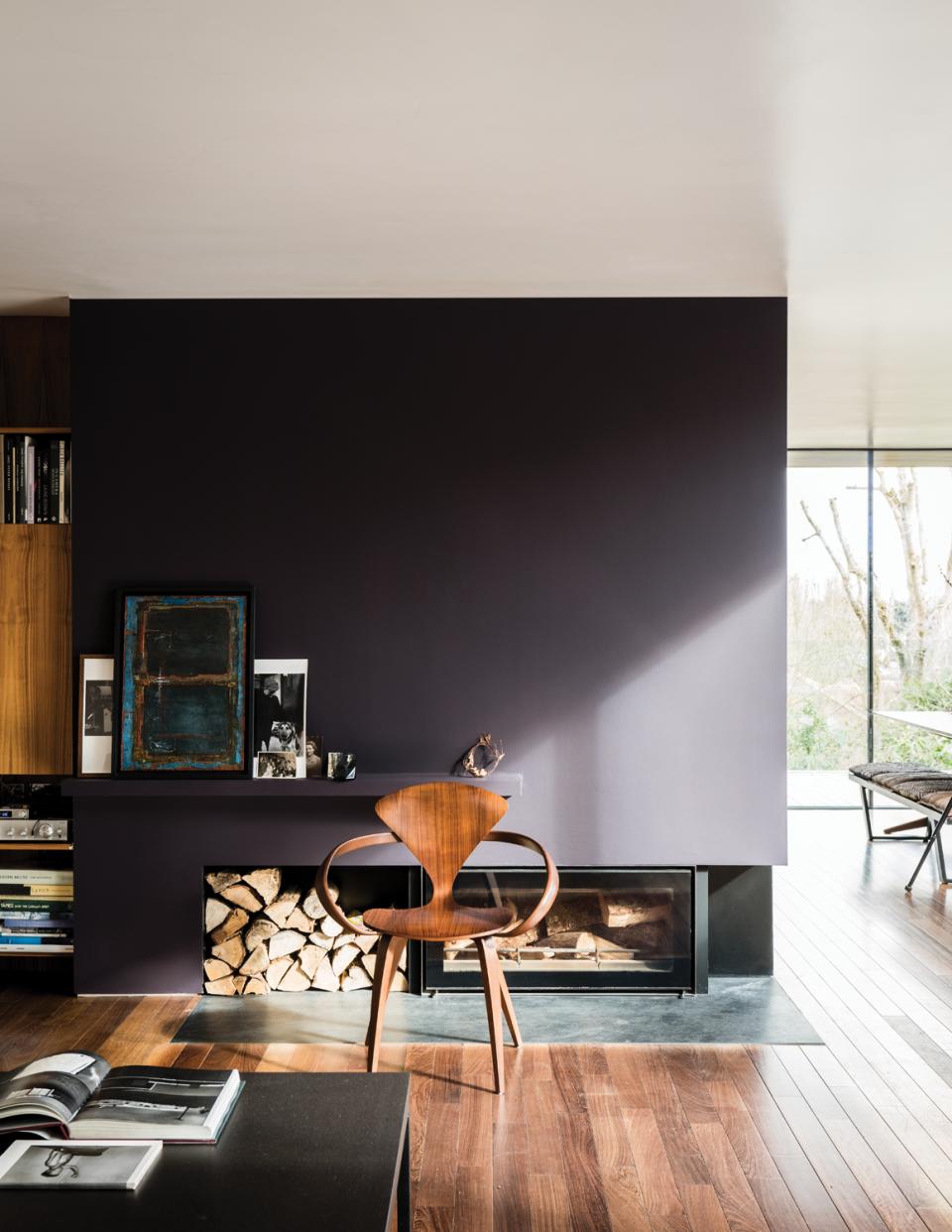 Modern living room featuring a dark-painted wall, wooden chair, and stylish fireplace, showcasing Farrow & Ball's new paint colors.