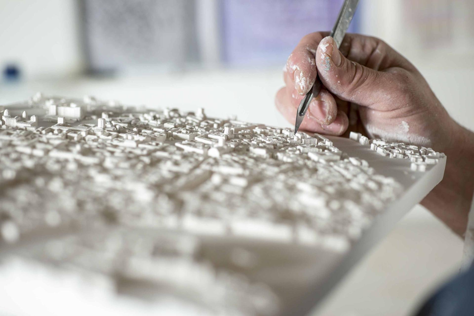 Artist detailing a three-dimensional model of an urban landscape, showcasing intricate city features and textures.
