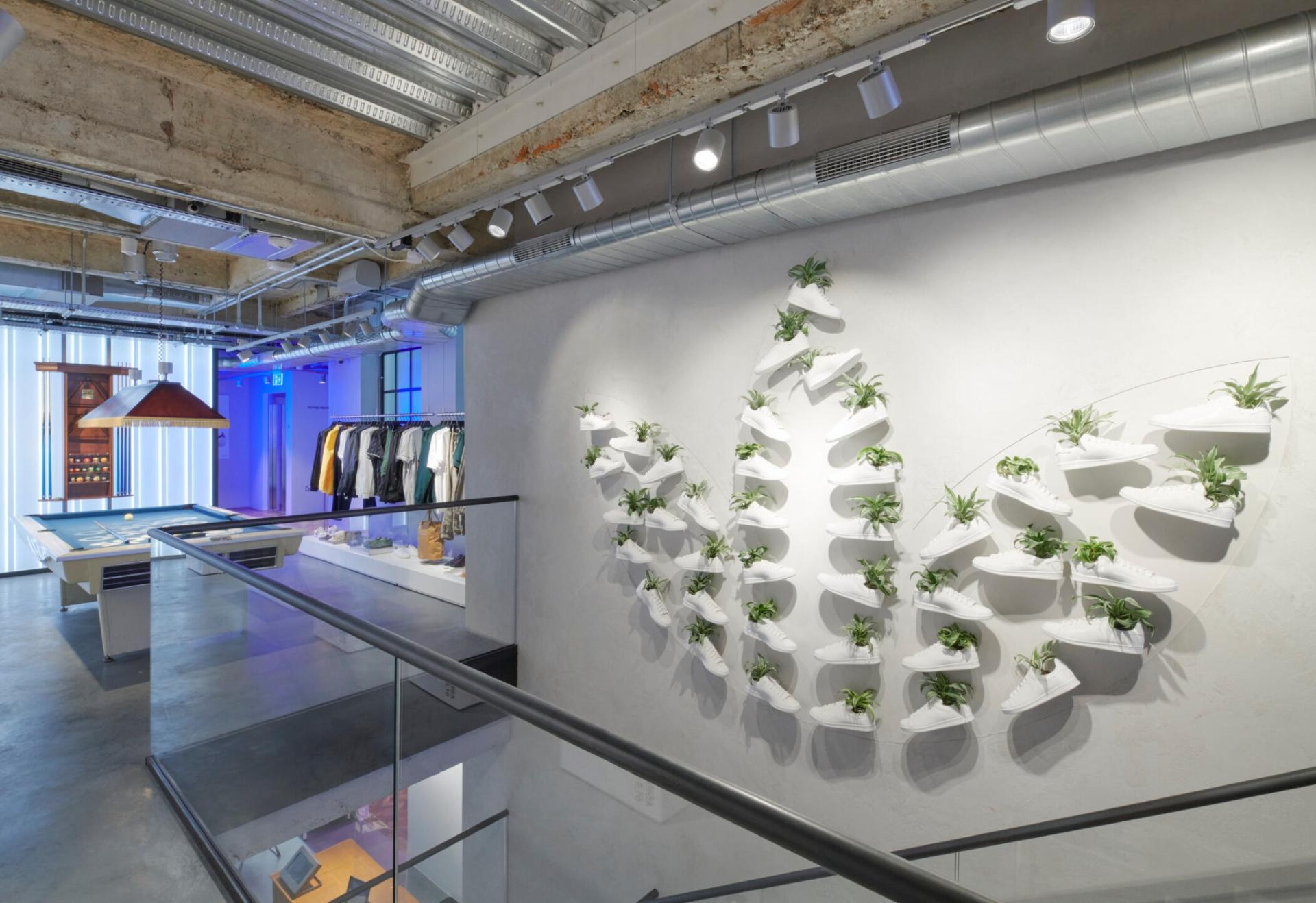 Sustainable vertical garden display featuring white Adidas shoes and plants in the flagship store interior.