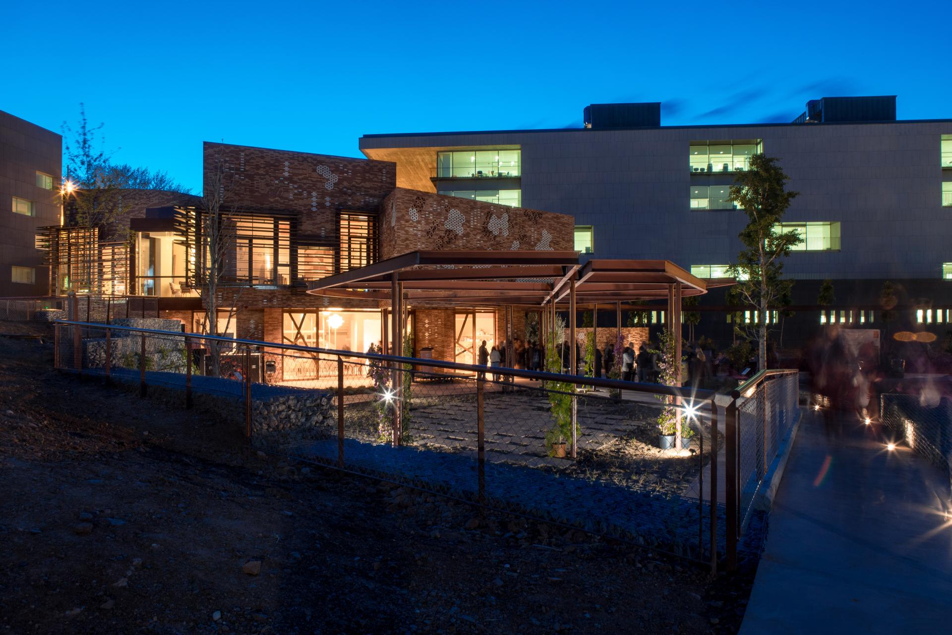 Modern Kālida Sant Pau building in Barcelona, featuring thermally modified tulipwood and illuminated outdoor spaces at dusk.