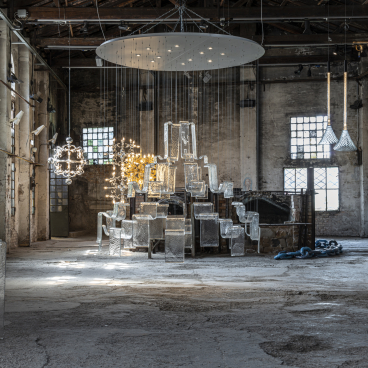 Clear glass furniture and lighting installations showcased in a rustic industrial space at the GLASS to GLASS exhibit.